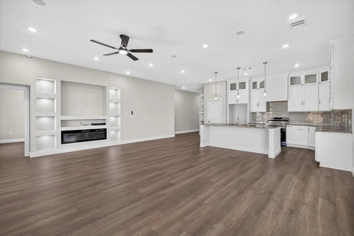 Expansive living space featuring wood-finish flooring, a built-in media center with shelving, and an electric fireplace