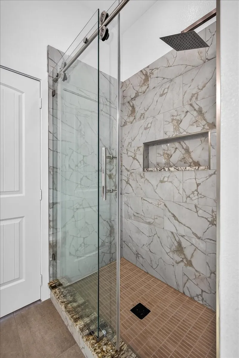 Glass-enclosed shower featuring a sliding barn door, rain showerhead, tiled walls with integrated niche, and a tiled shower floor