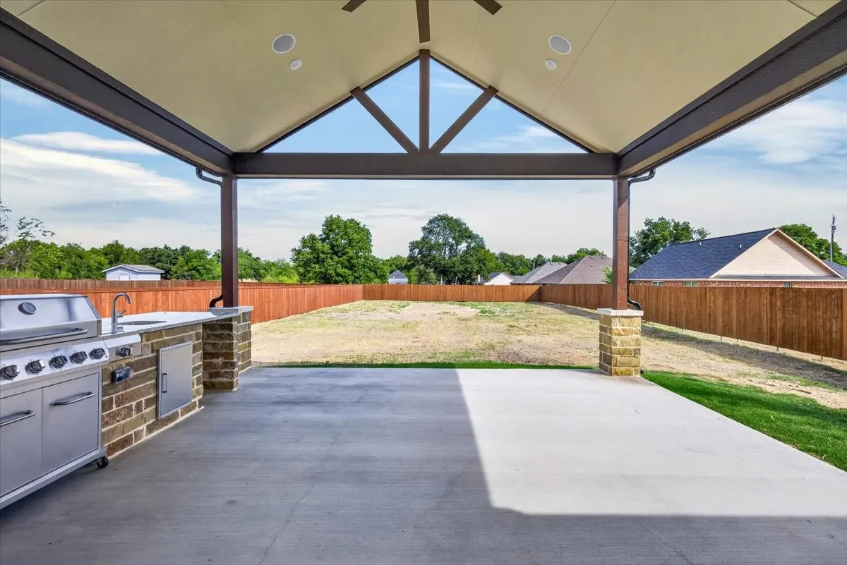 Covered patio with an outdoor kitchen, built-in grill, and a fenced backyard