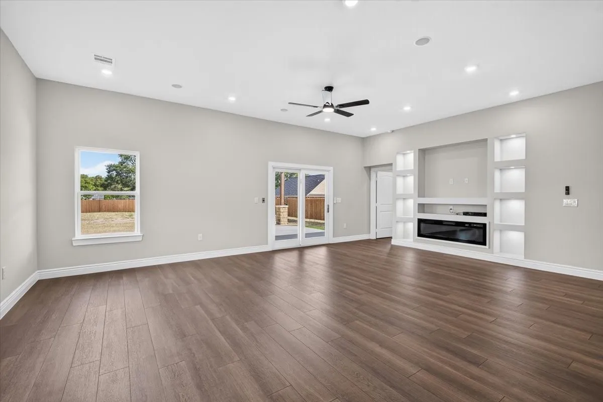 Spacious living area featuring wood-finish flooring, recessed lighting, and a built-in media center with illuminated shelving