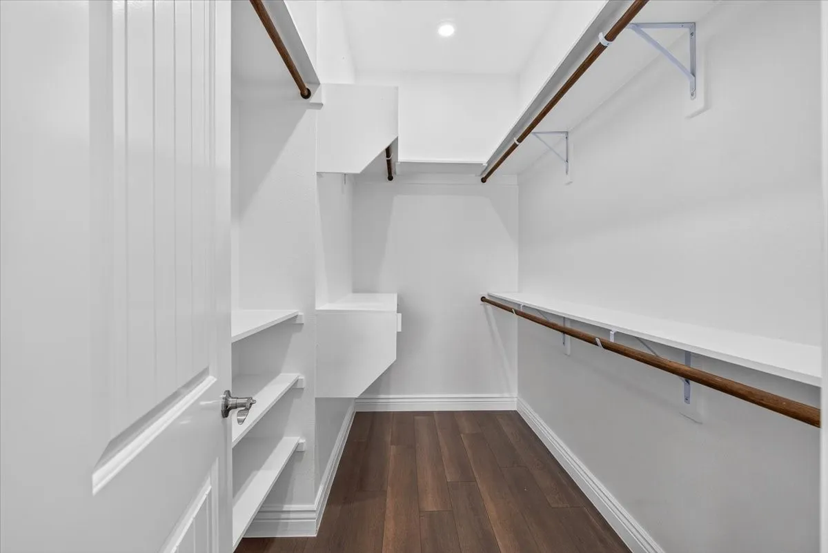 White paneled door opening to a walk-in closet featuring wood-finish flooring, recessed lighting, and built-in shelving with hanging rods