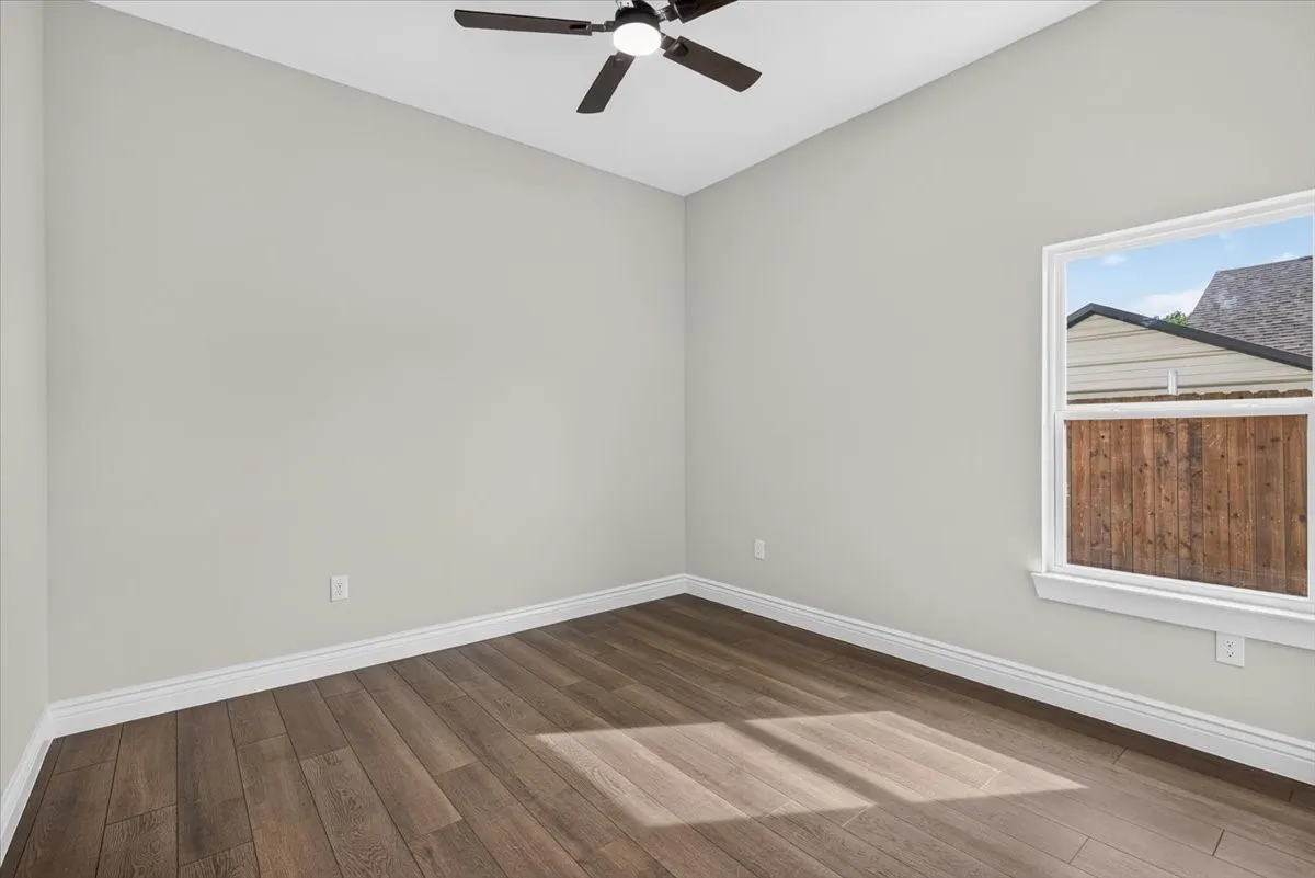 Spacious room featuring wood-finish flooring, light neutral wall paint, a ceiling fan with integrated lighting, and a white-framed window