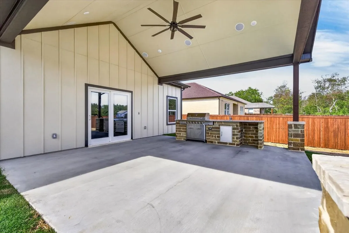 Expansive covered patio featuring a built-in outdoor kitchen, concrete flooring, dual French doors, and ceiling fan