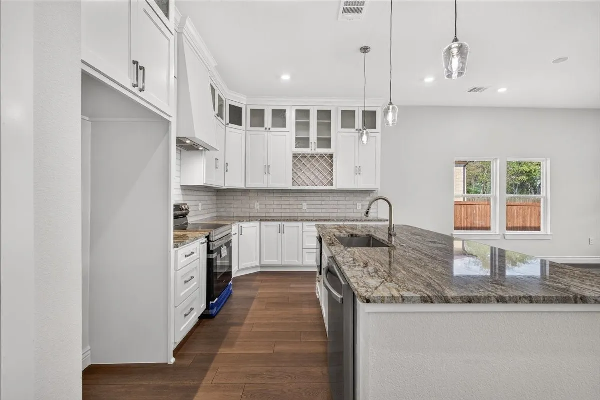 Modern kitchen featuring an expansive island with a built-in sink, stainless steel appliances, white cabinetry, and wood-finish flooring