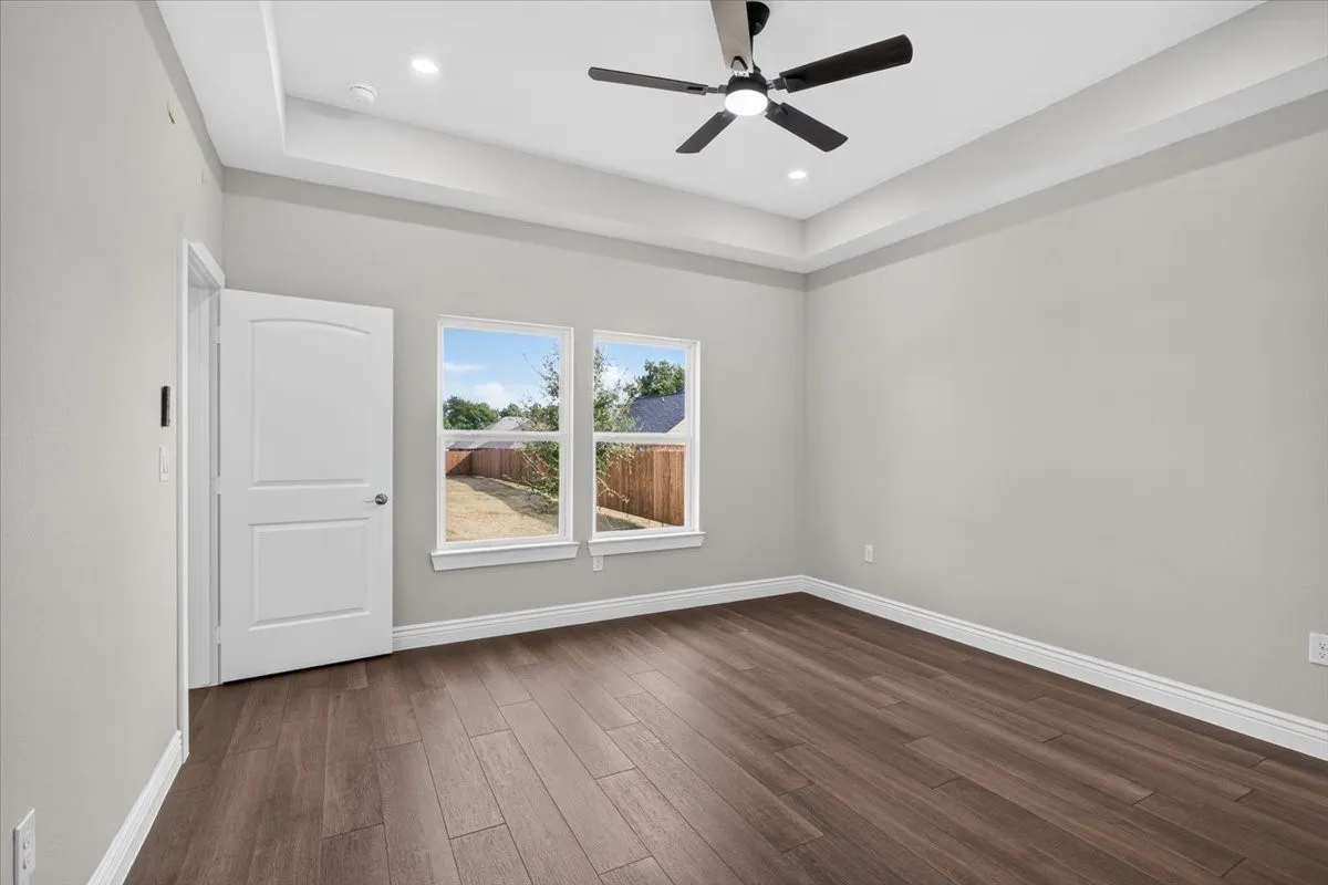 Tray ceiling with recessed lighting and a ceiling fan, wood-finish flooring, and two windows
