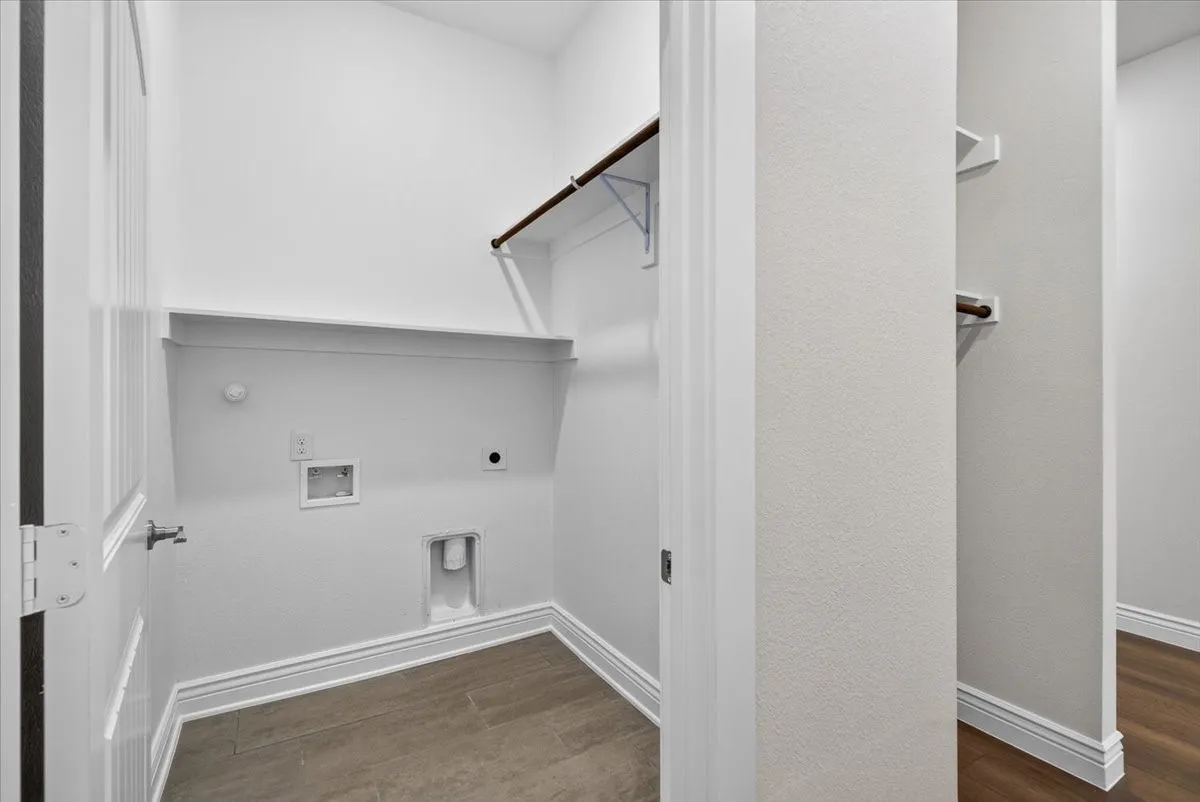 Dedicated utility space featuring wood-finish flooring, built-in shelving, and a clothing rod