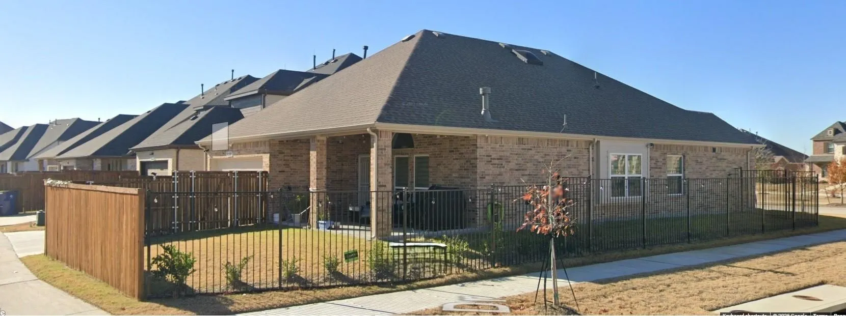 Brick exterior with gabled roof, covered patio, and metal fencing