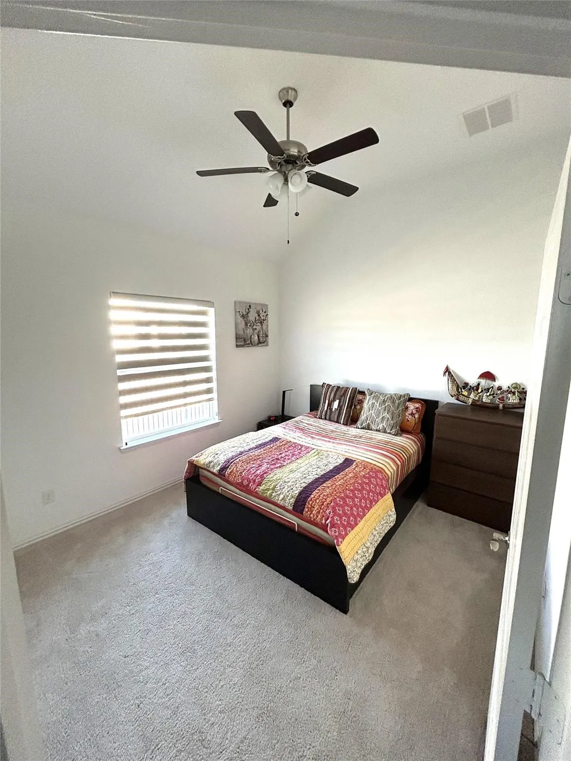 Carpeted bedroom featuring a ceiling fan with integrated lighting, a window with horizontal blinds, and a built-in air vent