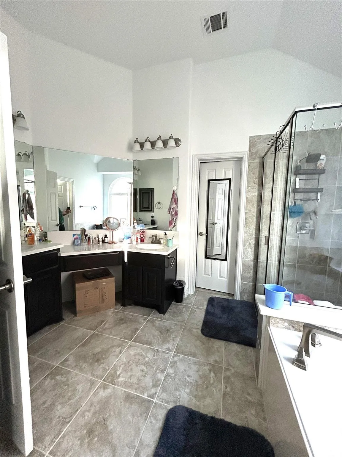 Dual vanity with dark wood-finish cabinetry, tile flooring, walk-in shower with glass enclosure, separate bathtub, and vaulted ceiling