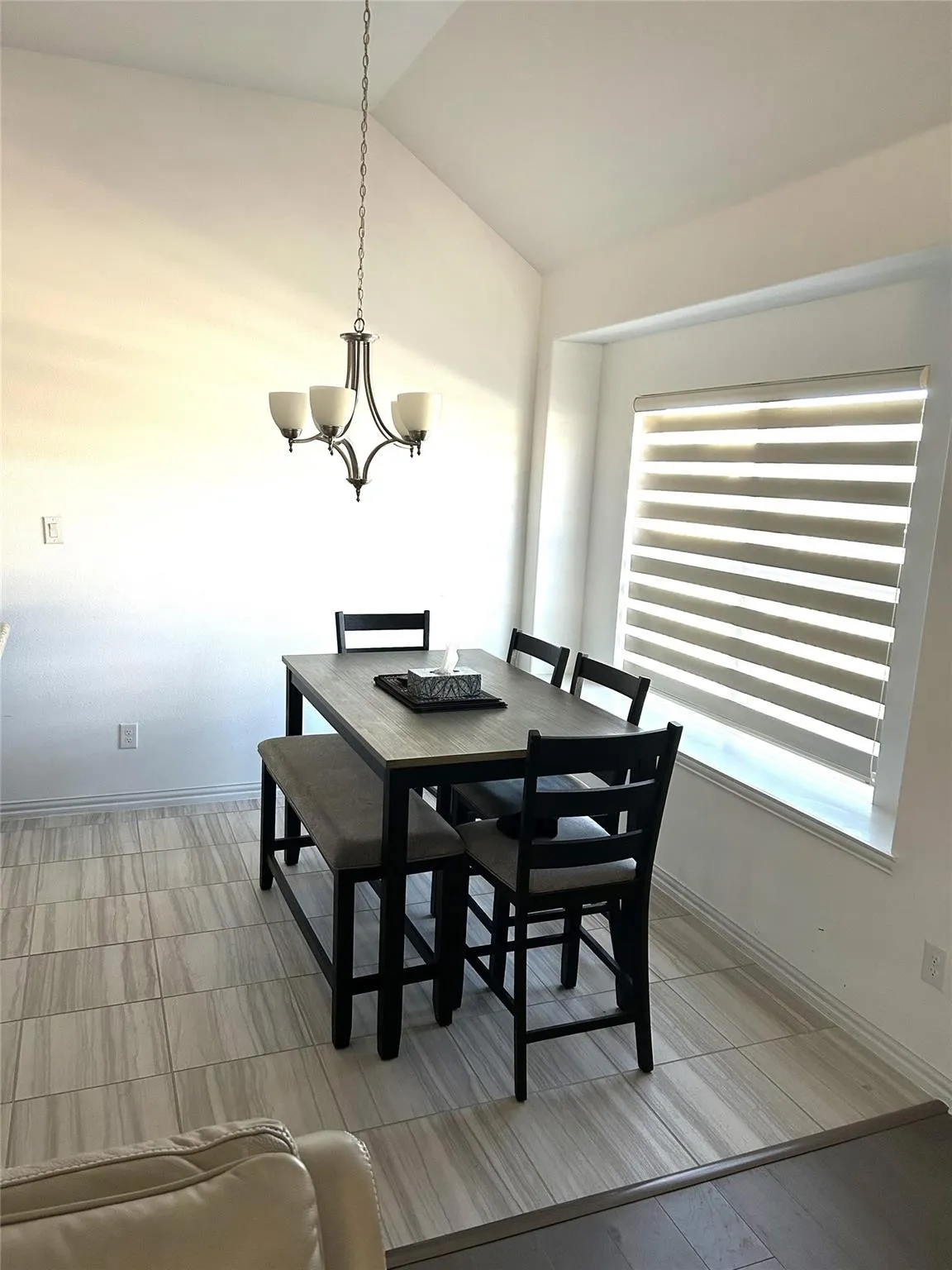 Vaulted ceiling with a chandelier, large window with blinds, and tile flooring