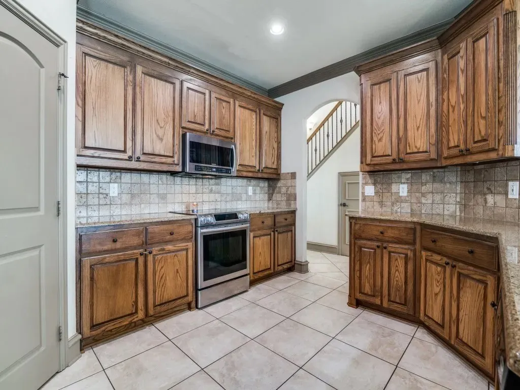 Kitchen featuring wood cabinetry, stainless steel appliances, tiled backsplash, and light-toned floor tiles