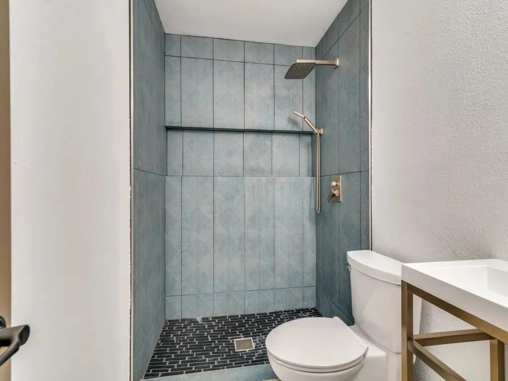 Walk-in shower with blue patterned tile walls, built-in shelving, and a mosaic tile floor
