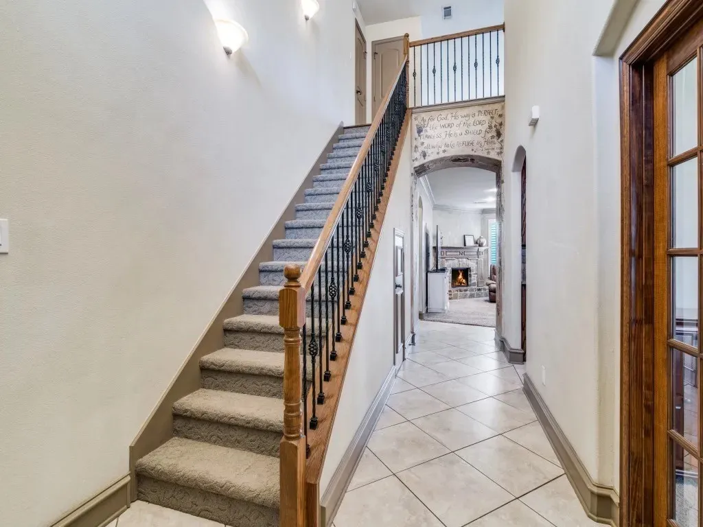 Carpeted staircase with wrought iron and wood balusters, tile flooring, arched doorway, and wood-paneled door