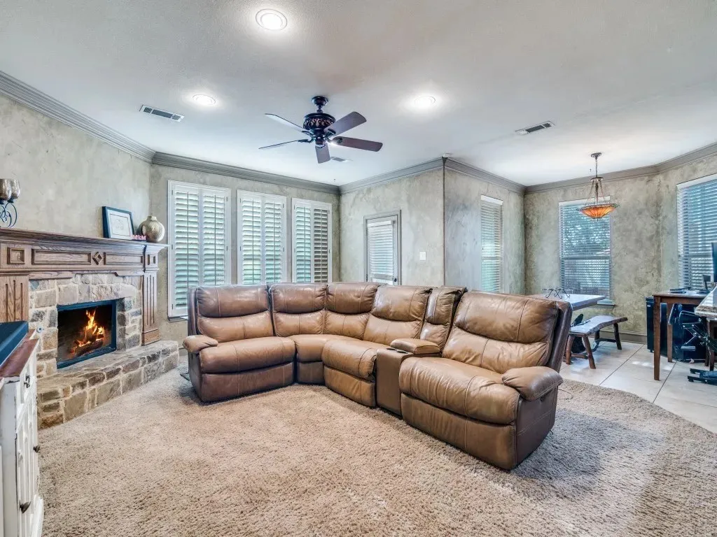 Stone-surround fireplace with a wood mantle, crown molding, plantation shutters, recessed lighting, and a ceiling fan