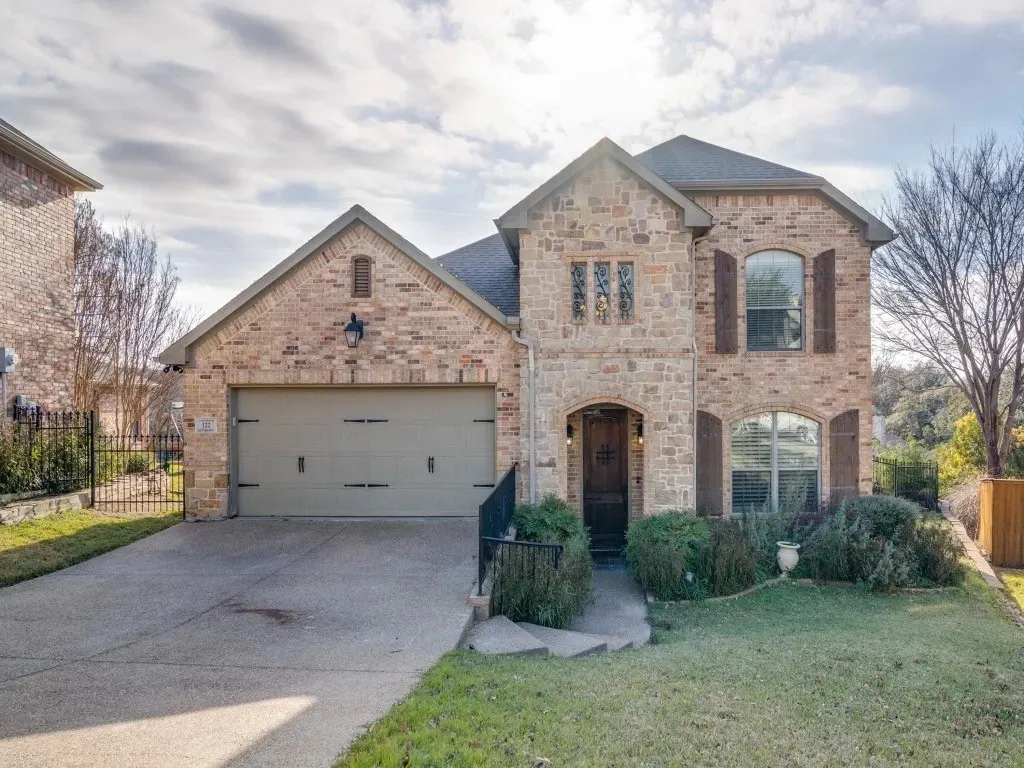 Stone and brick facade with a two-car garage, arched entry, and decorative shutters
