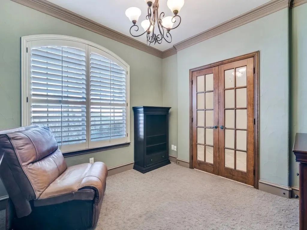 Arched window with plantation shutters, double French doors, crown molding, chandelier lighting, and carpeting