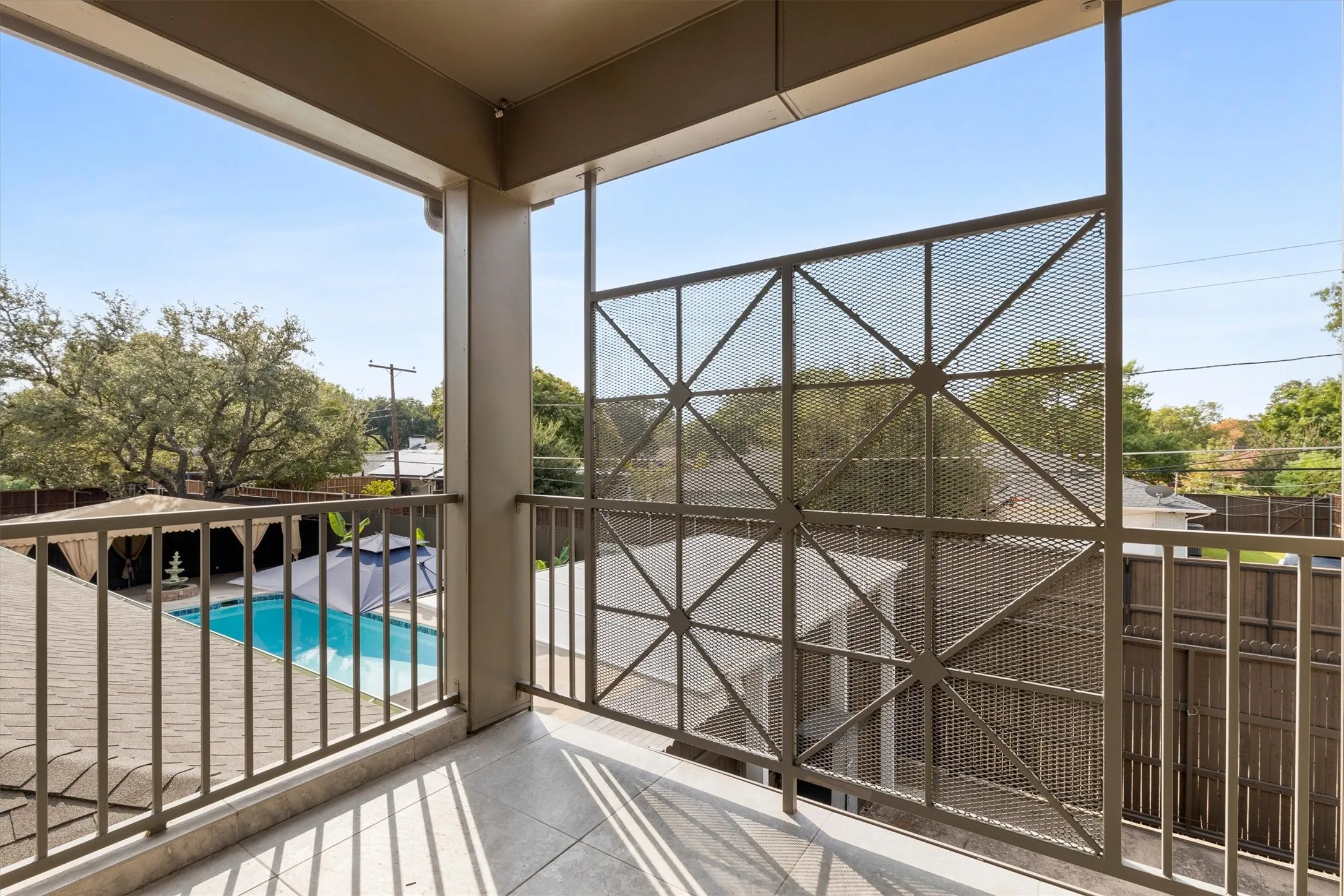 Balcony with a metal railing and privacy screen, overlooking a swimming pool and covered patio