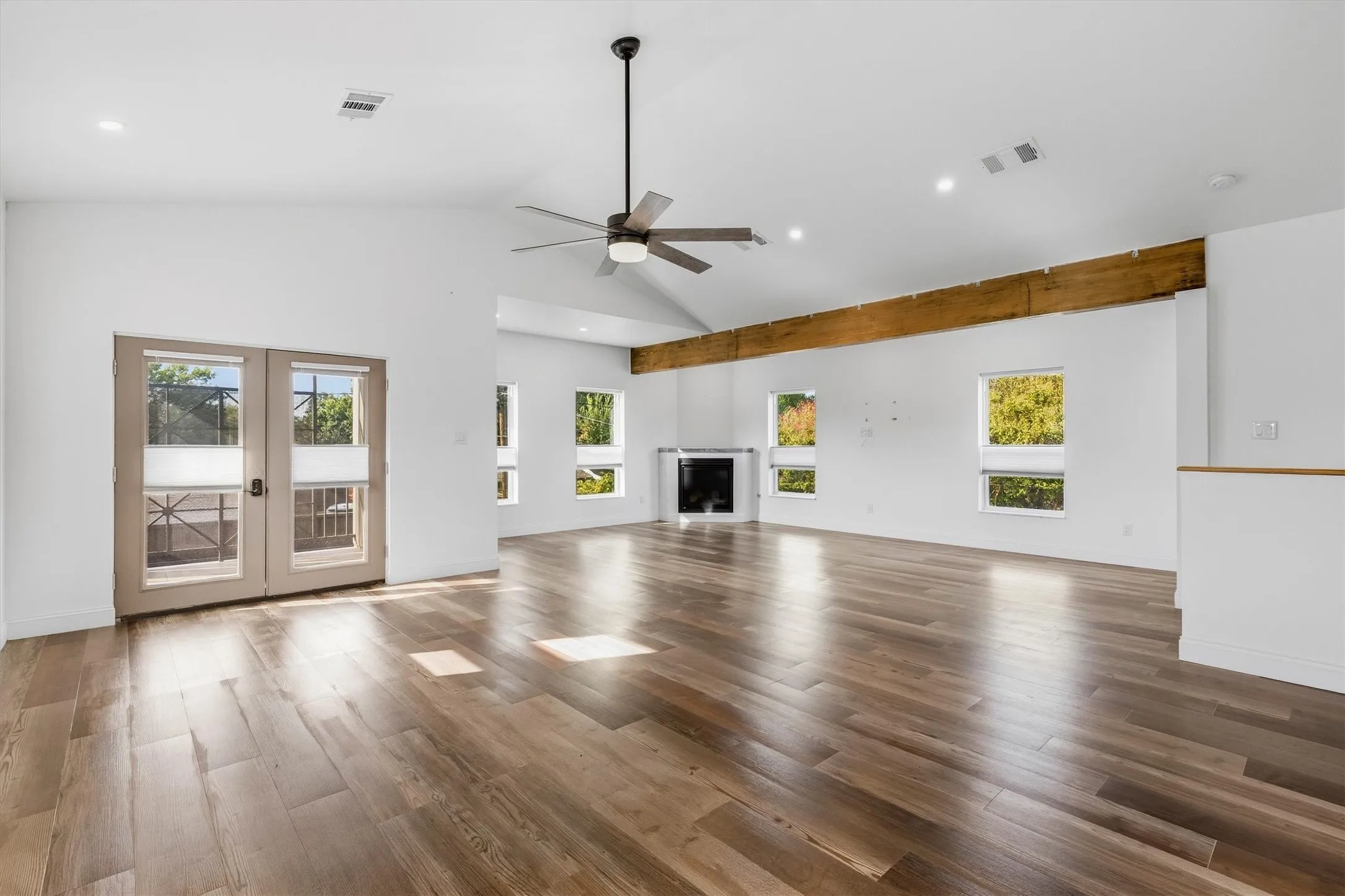 Vaulted ceiling, wood-finish flooring, exposed wood beam, modern fireplace, and double French doors to outdoor space