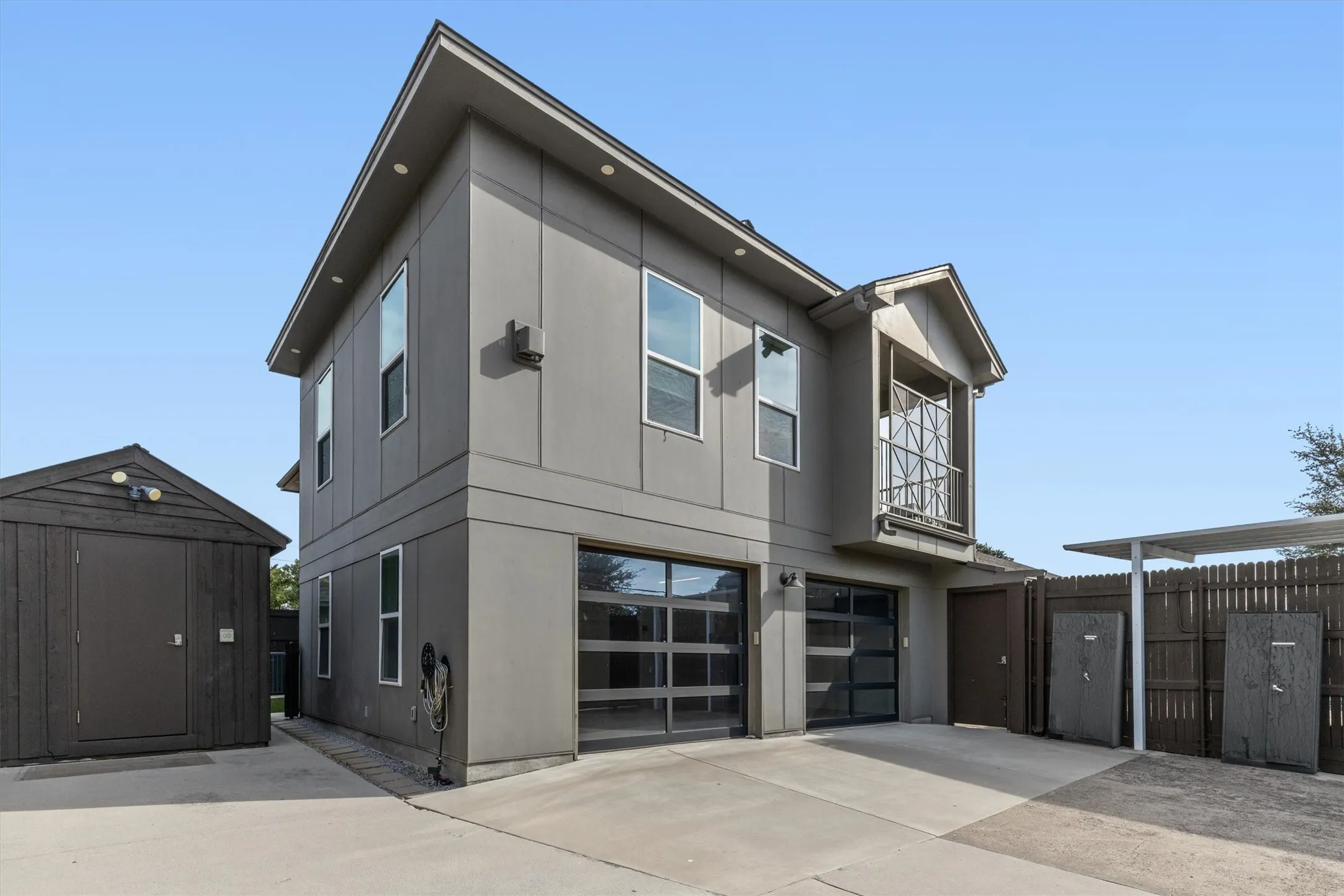 Two-story exterior with a balcony, two glass-paneled garage doors, an exterior storage shed, and a covered outdoor area