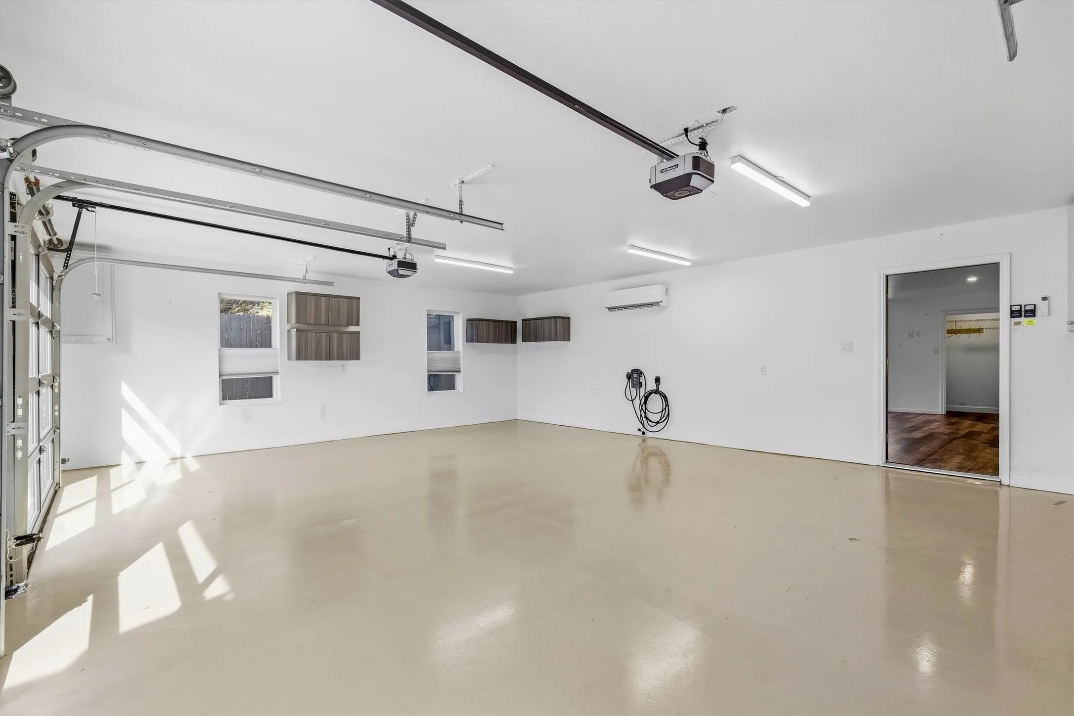 Spacious garage with an overhead door, multiple windows, built-in wall cabinets, and fluorescent ceiling lighting