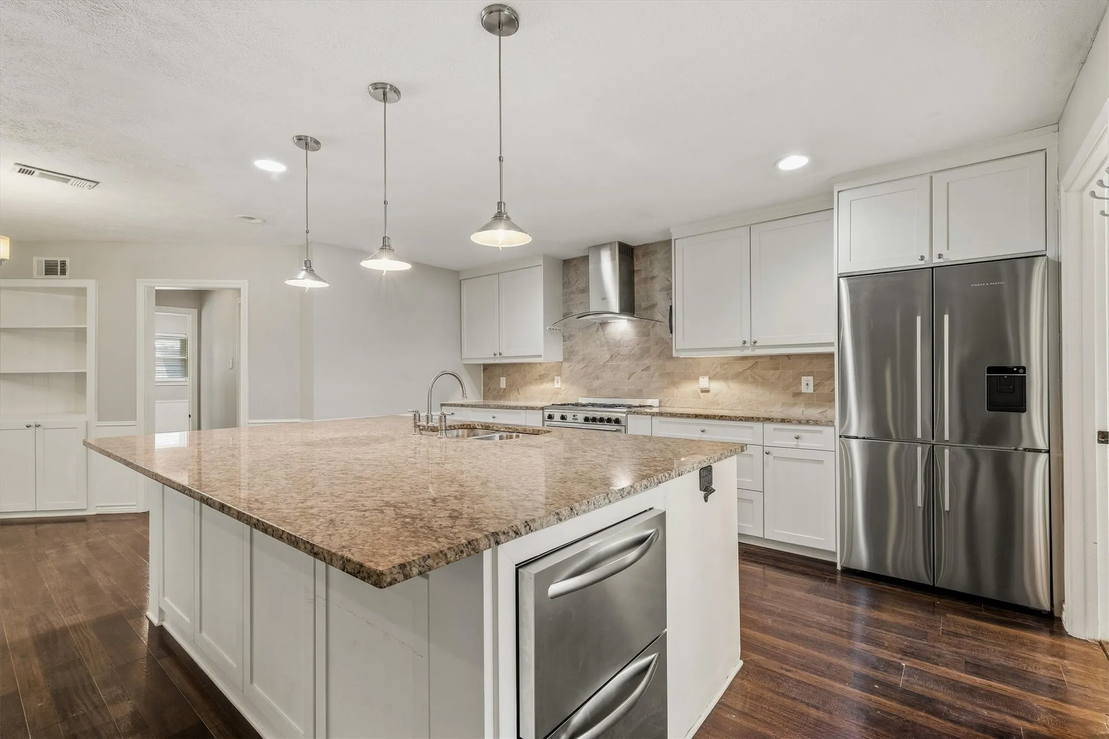 Expansive kitchen island with a stone countertop, white shaker cabinetry, stainless steel appliances, and dark wood-finish flooring