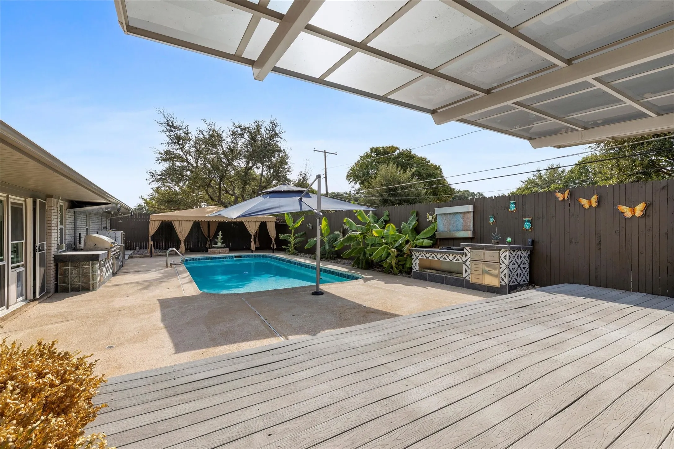 Expansive outdoor area featuring a swimming pool, wood deck, covered patio, built-in outdoor kitchen, and privacy fencing