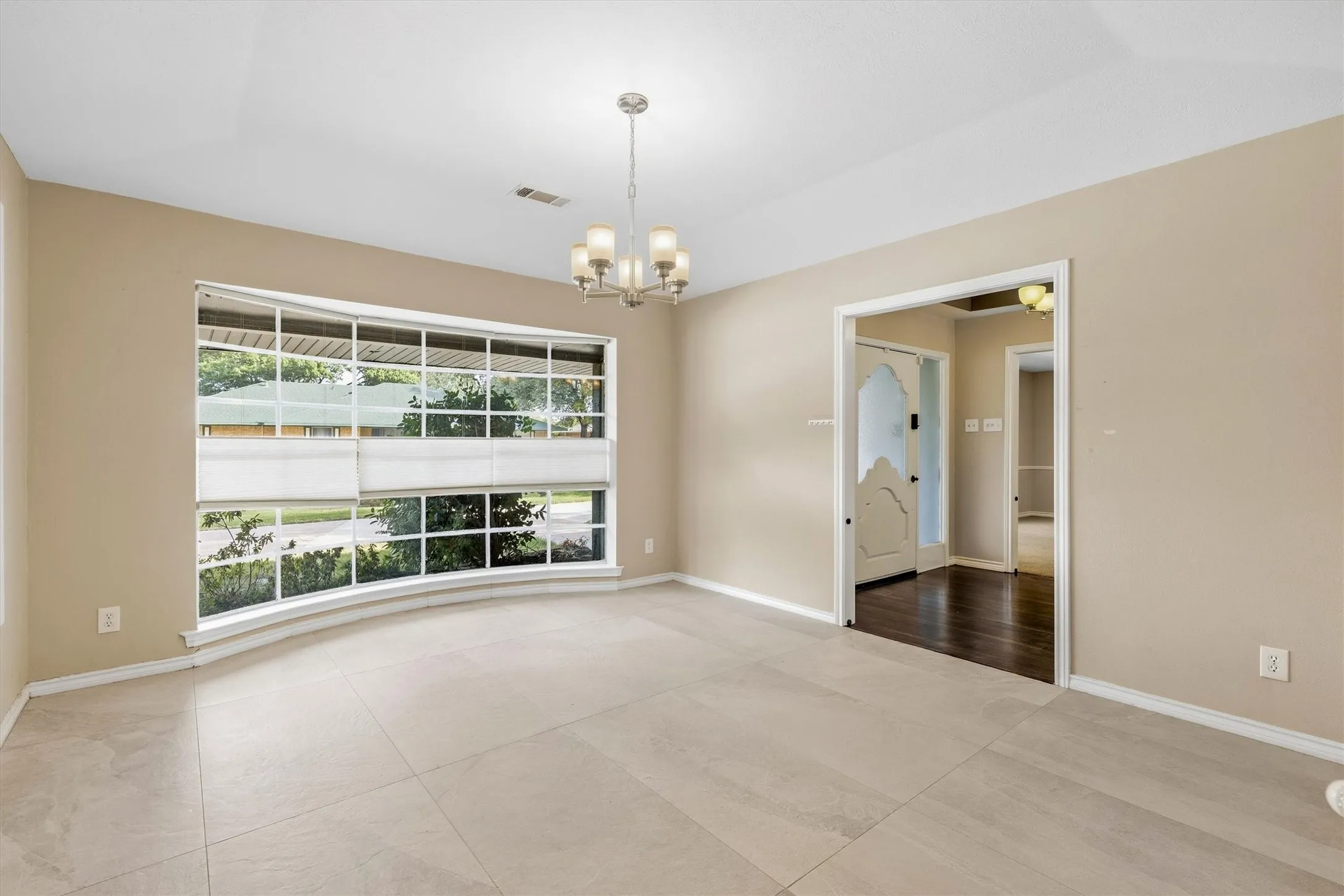 Recessed ceiling with a chandelier, bay window, light-toned tile flooring, and a decorative interior door