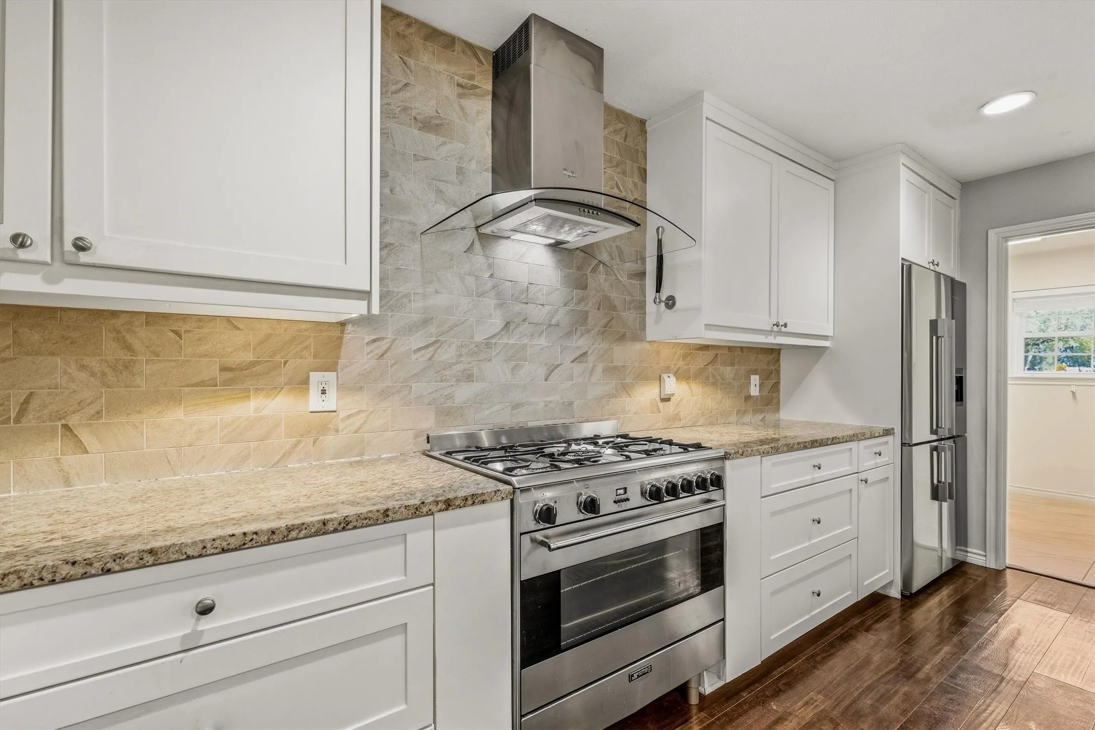 Kitchen featuring white cabinetry, granite countertops, stainless steel appliances, a tile backsplash, and wood-finish flooring