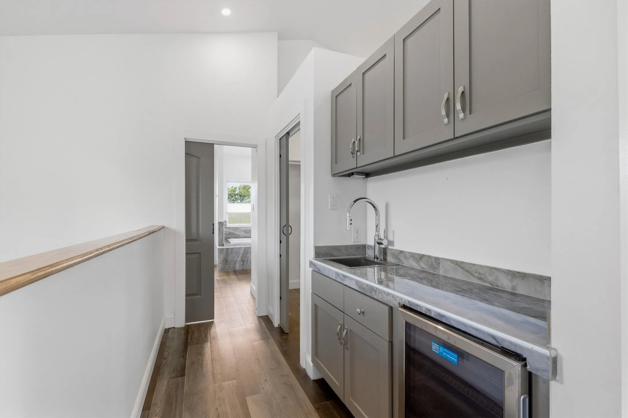 Wood-finish flooring, recessed lighting, built-in cabinetry with a sink, stone countertop, and an integrated beverage refrigerator