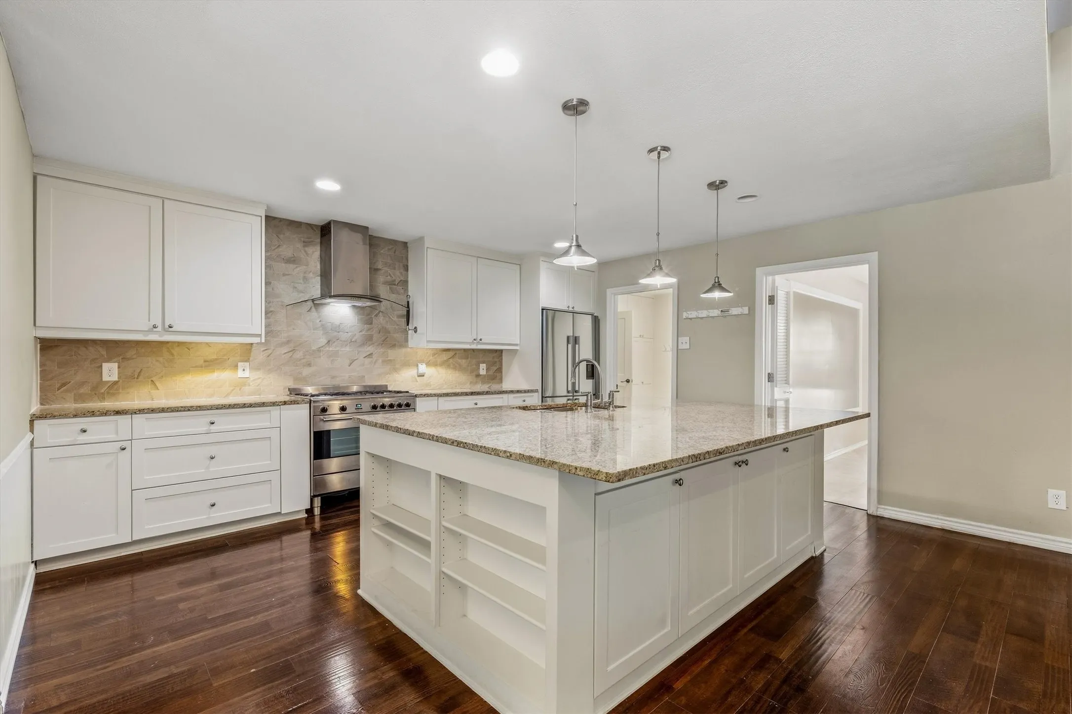 Kitchen featuring an expansive island with a stone countertop, white shaker cabinetry, stainless steel range with matching hood, and wood-finish flooring