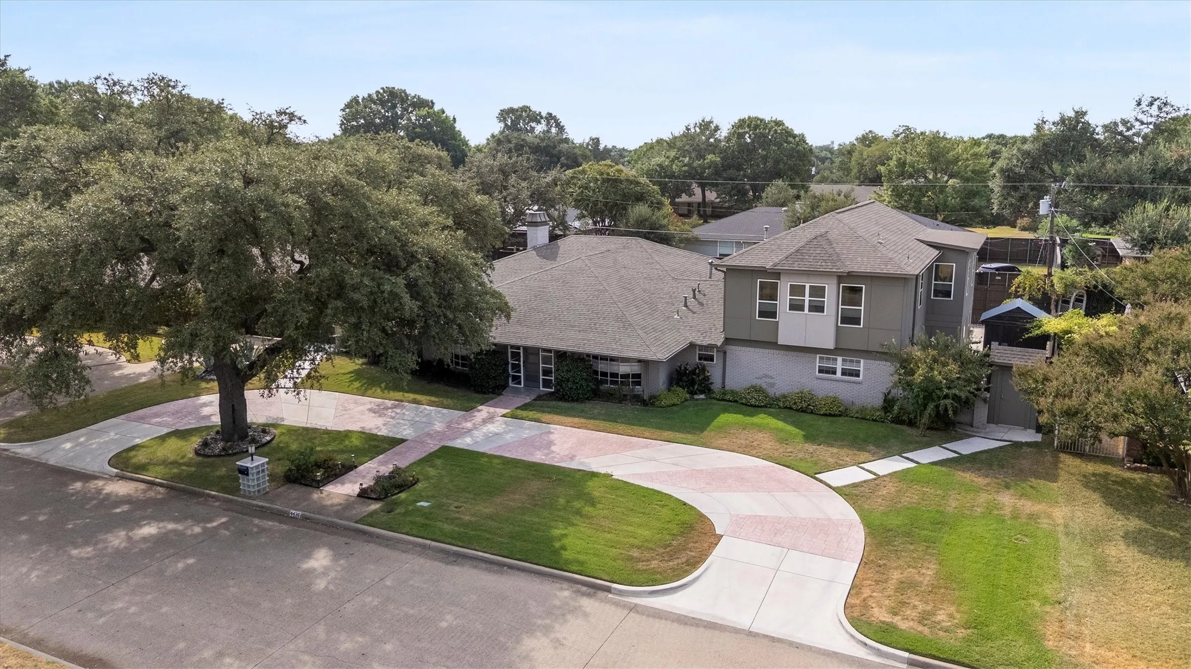 Expansive circular driveway with patterned paving, mature front yard tree, and an additional side entrance