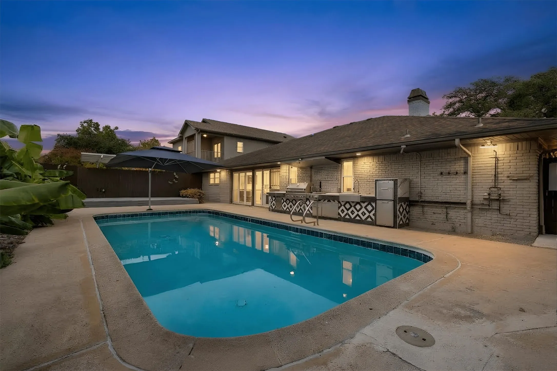 Backyard with a rectangular swimming pool, concrete decking, an outdoor kitchen with built-in appliances, and a brick-faced exterior