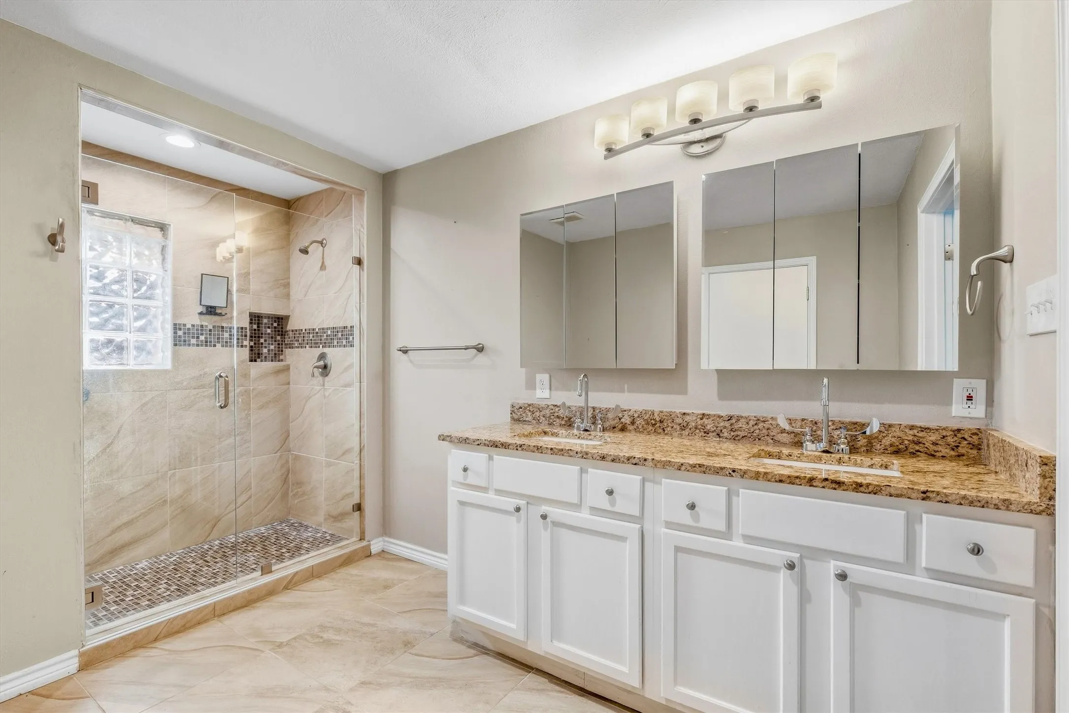 Dual vanity with granite countertops, tile flooring, glass-enclosed shower, mosaic tile accents, and recessed shower lighting