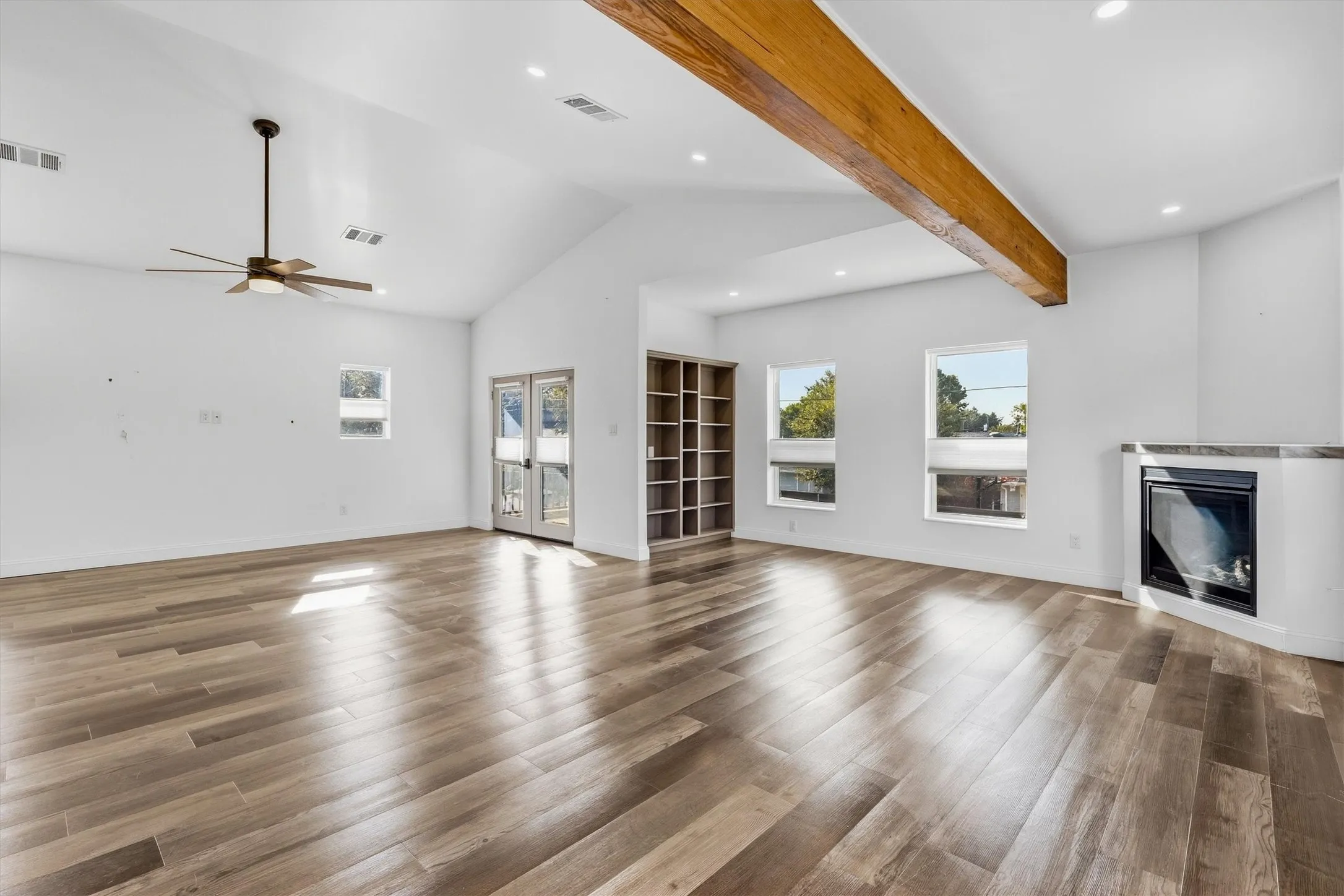 Vaulted ceilings with exposed wood beam, wood-finish flooring, built-in shelving, fireplace, and french doors