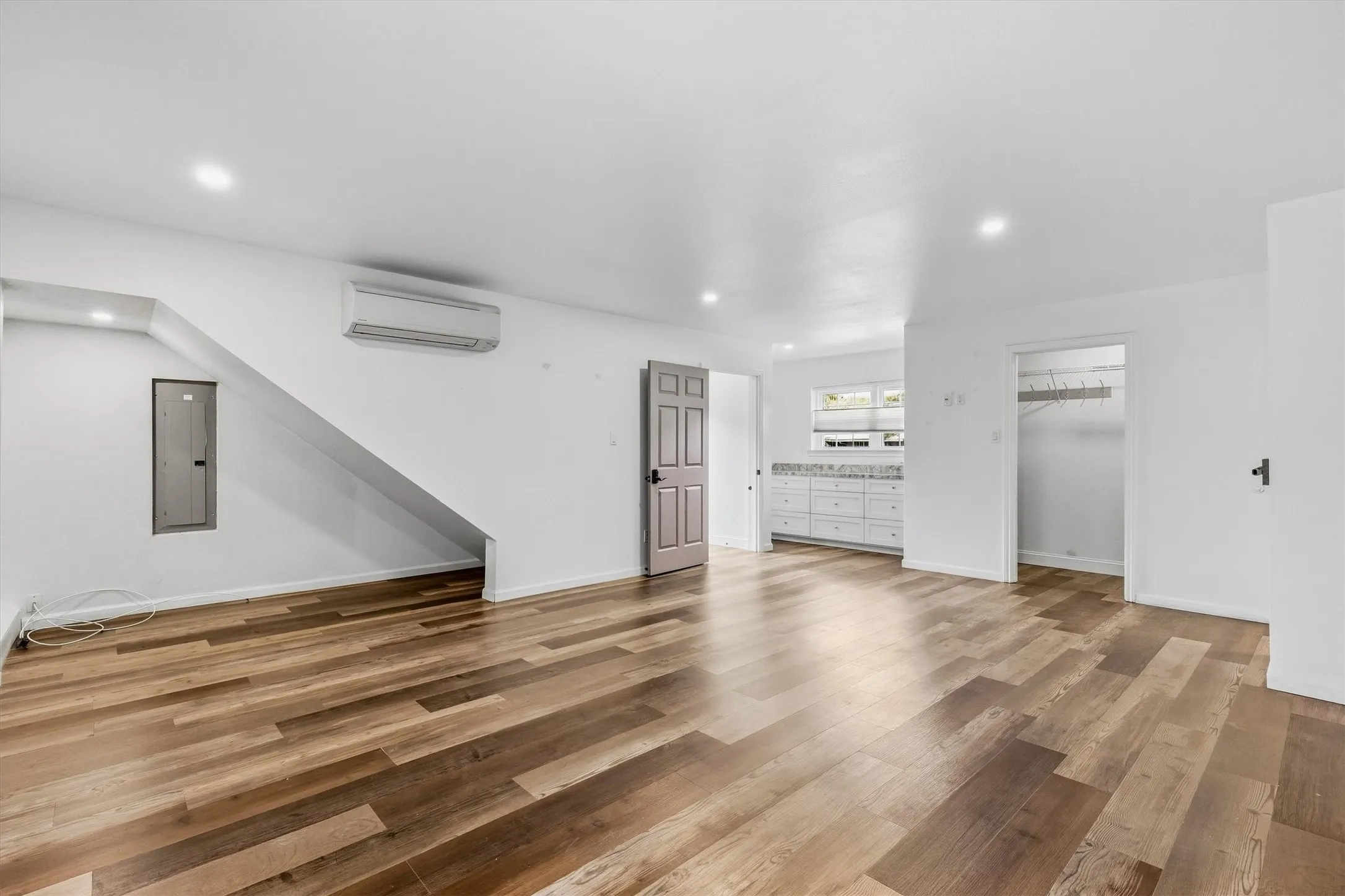 Wood-finish flooring, recessed lighting, white walls, built-in cabinetry with a light-colored countertop, and a wall-mounted climate control unit