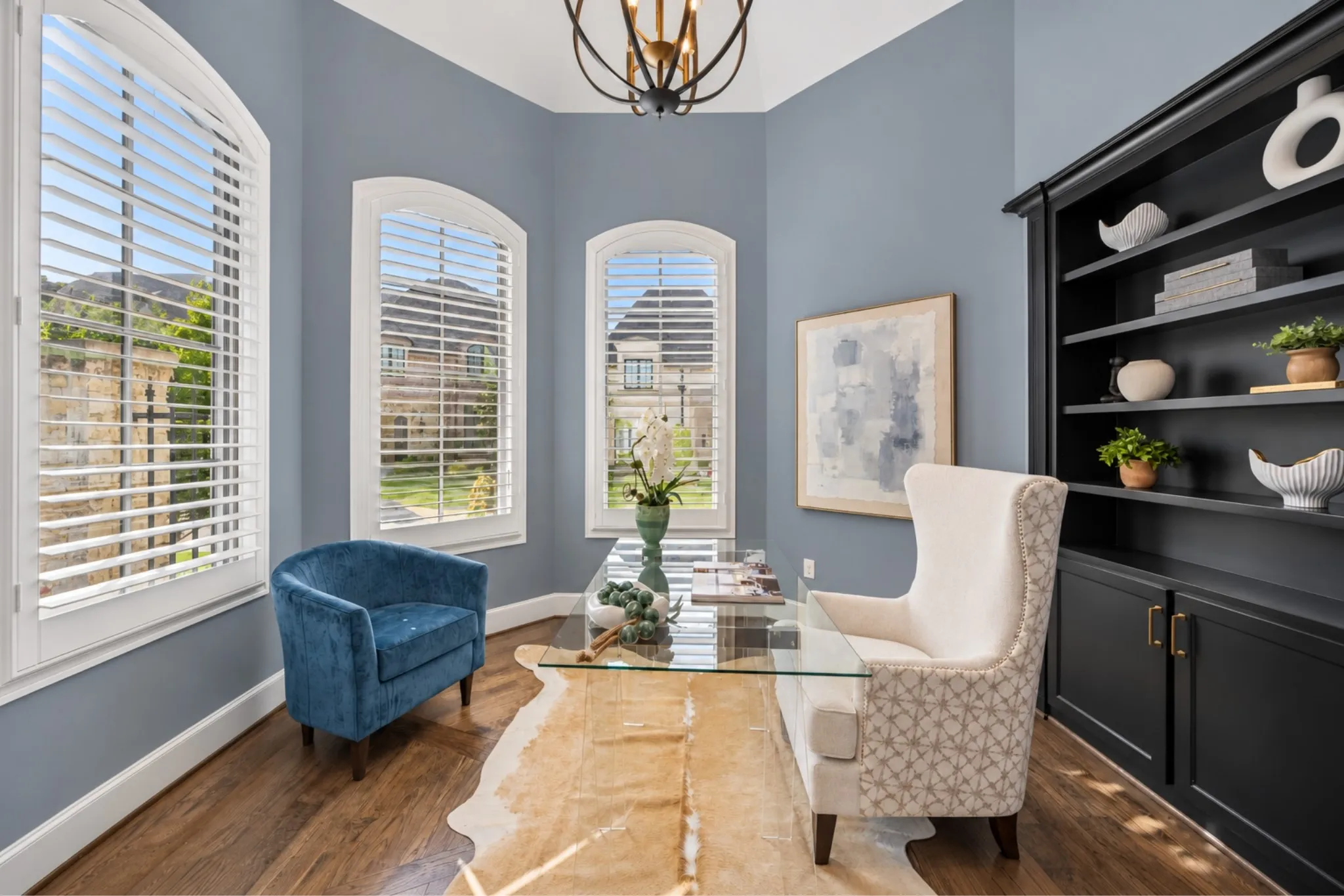 Arched windows with plantation shutters, wood-finish flooring, built-in shelving, and a decorative ceiling light fixture