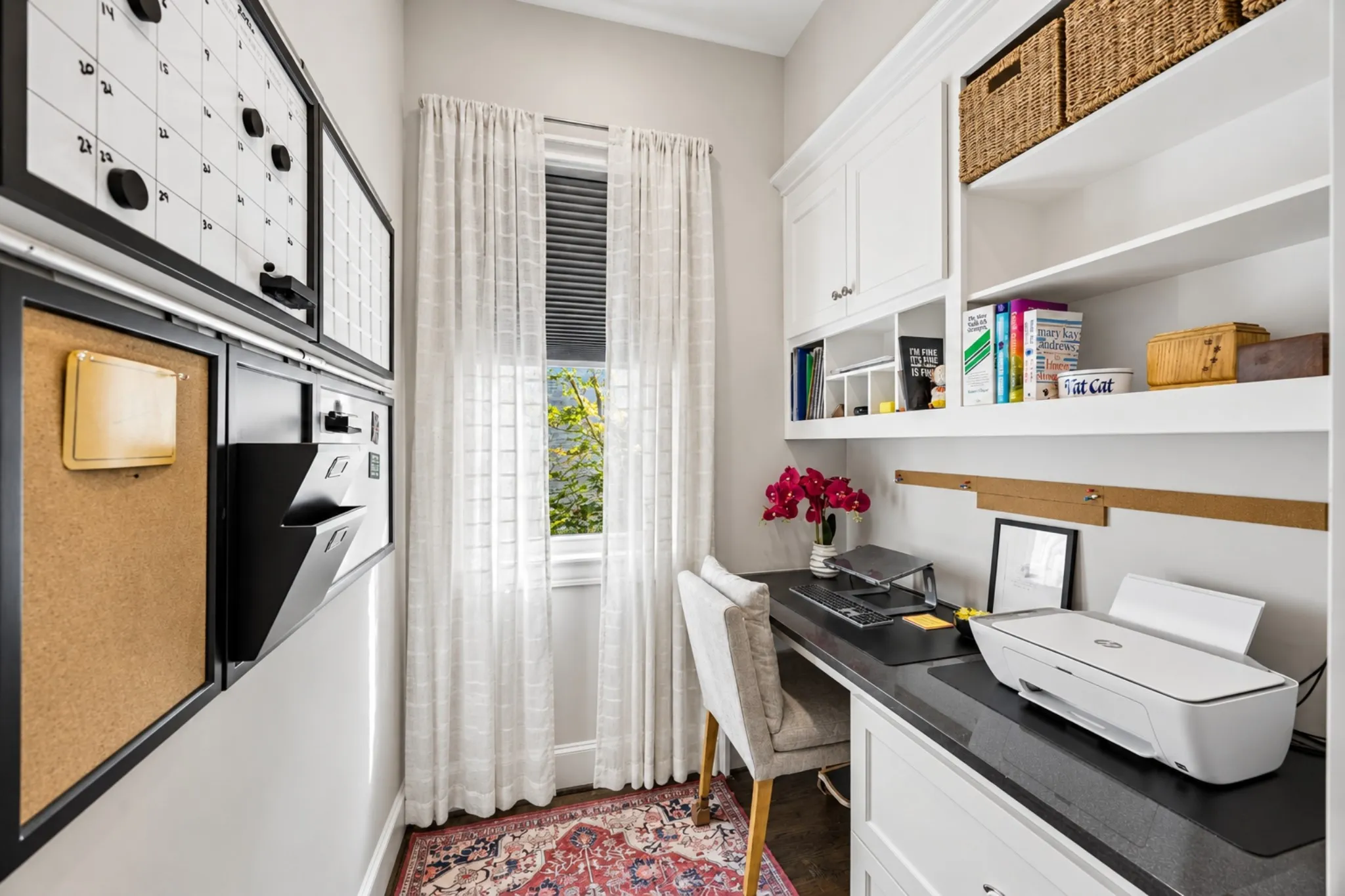 Built-in desk with dark countertop, white cabinetry with upper shelving, and a large window with privacy blinds