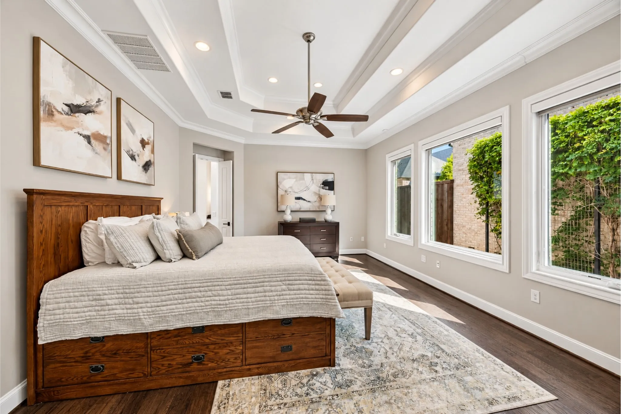 Tray ceiling with recessed lighting, dark wood-finish flooring, multiple windows, ceiling fan, and crown molding