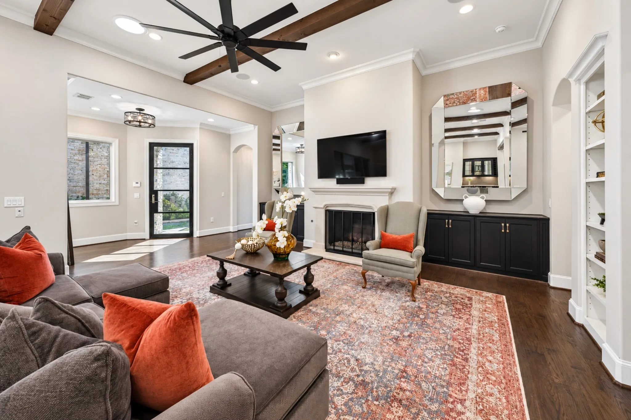 Living area featuring dark wood-finish flooring, exposed ceiling beams, a ceiling fan, and a fireplace with a mantel