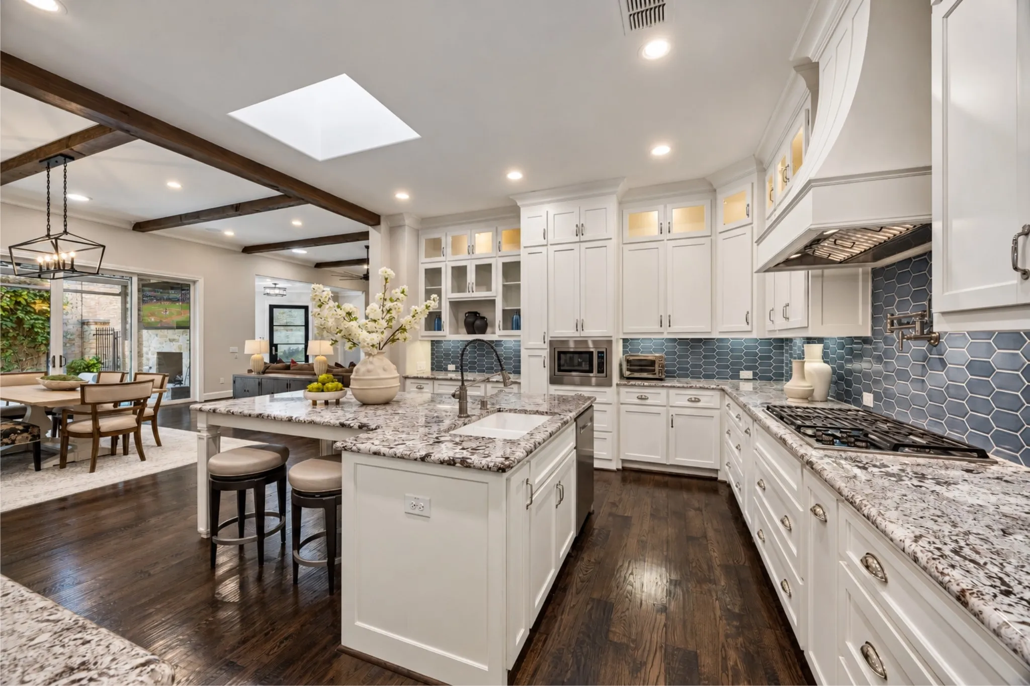 Kitchen featuring white cabinetry, light-toned countertops, a geometric blue tile backsplash, a central island with a sink, and dark wood-finish flooring
