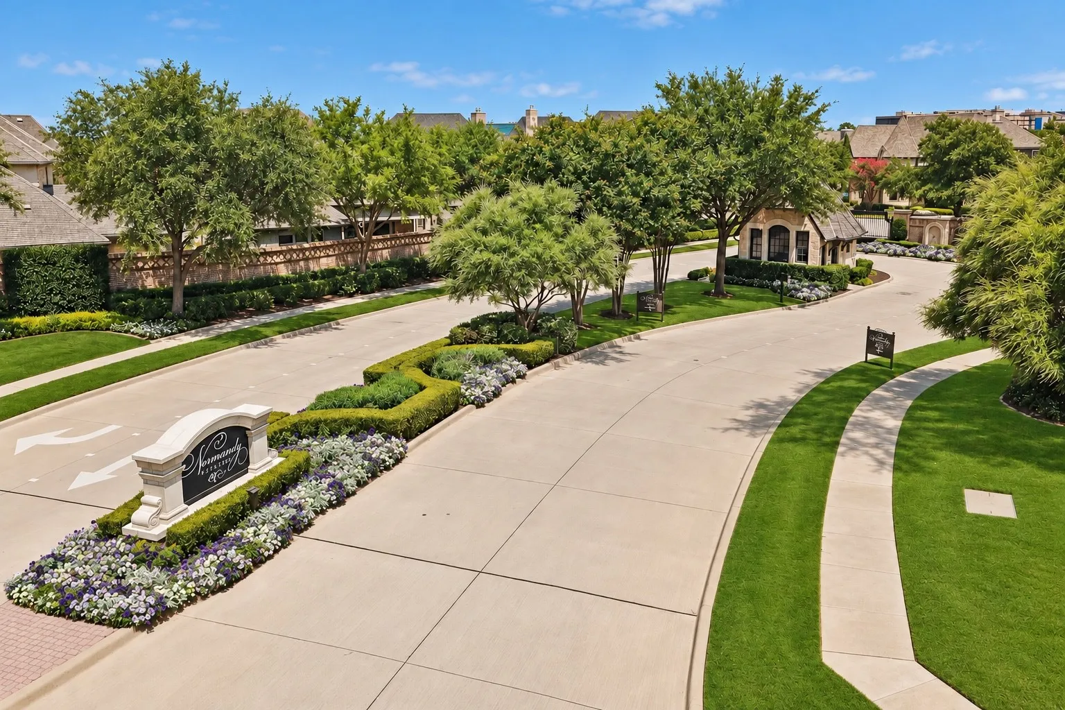 Landscaped entryway with a stone sign, manicured lawns, mature trees, and a stone-clad gatehouse