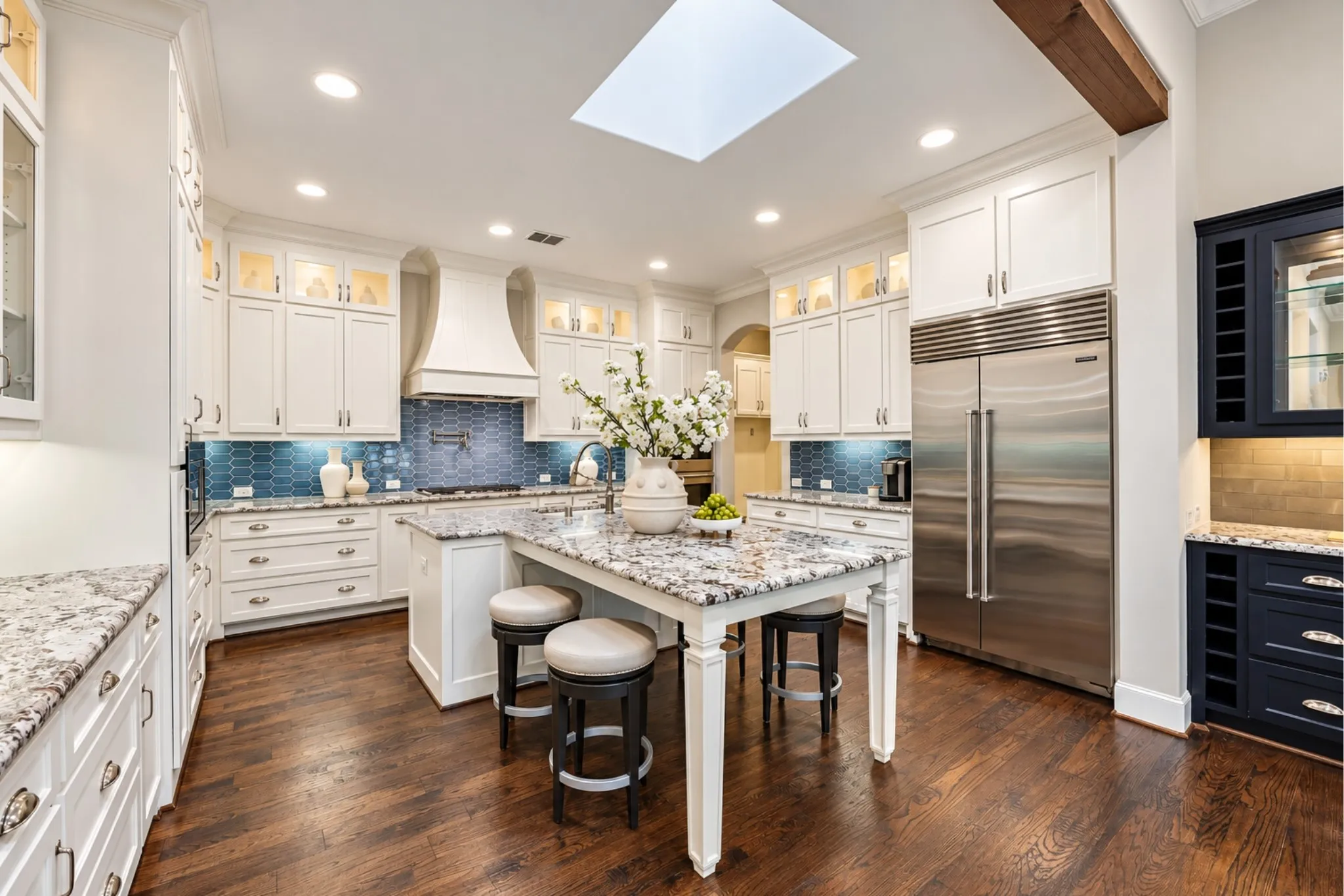 Gourmet kitchen featuring a large central island, white cabinetry, integrated stainless steel appliances, wood-finish flooring, and a skylight
