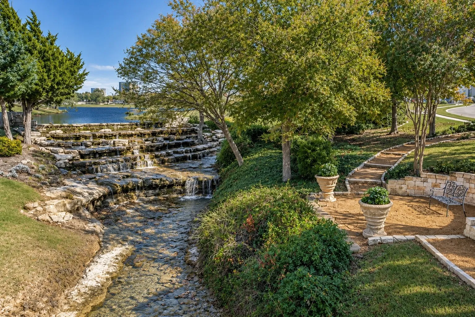 Tiered rock waterfall with a flowing stream, stone-lined pathways, and mature trees