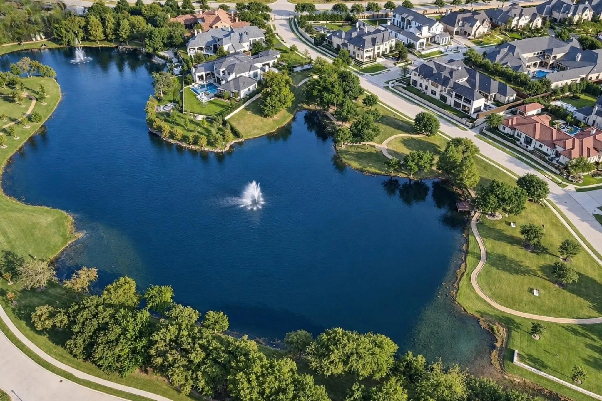Lakeside residences with manicured grounds, mature trees, and a tranquil water feature