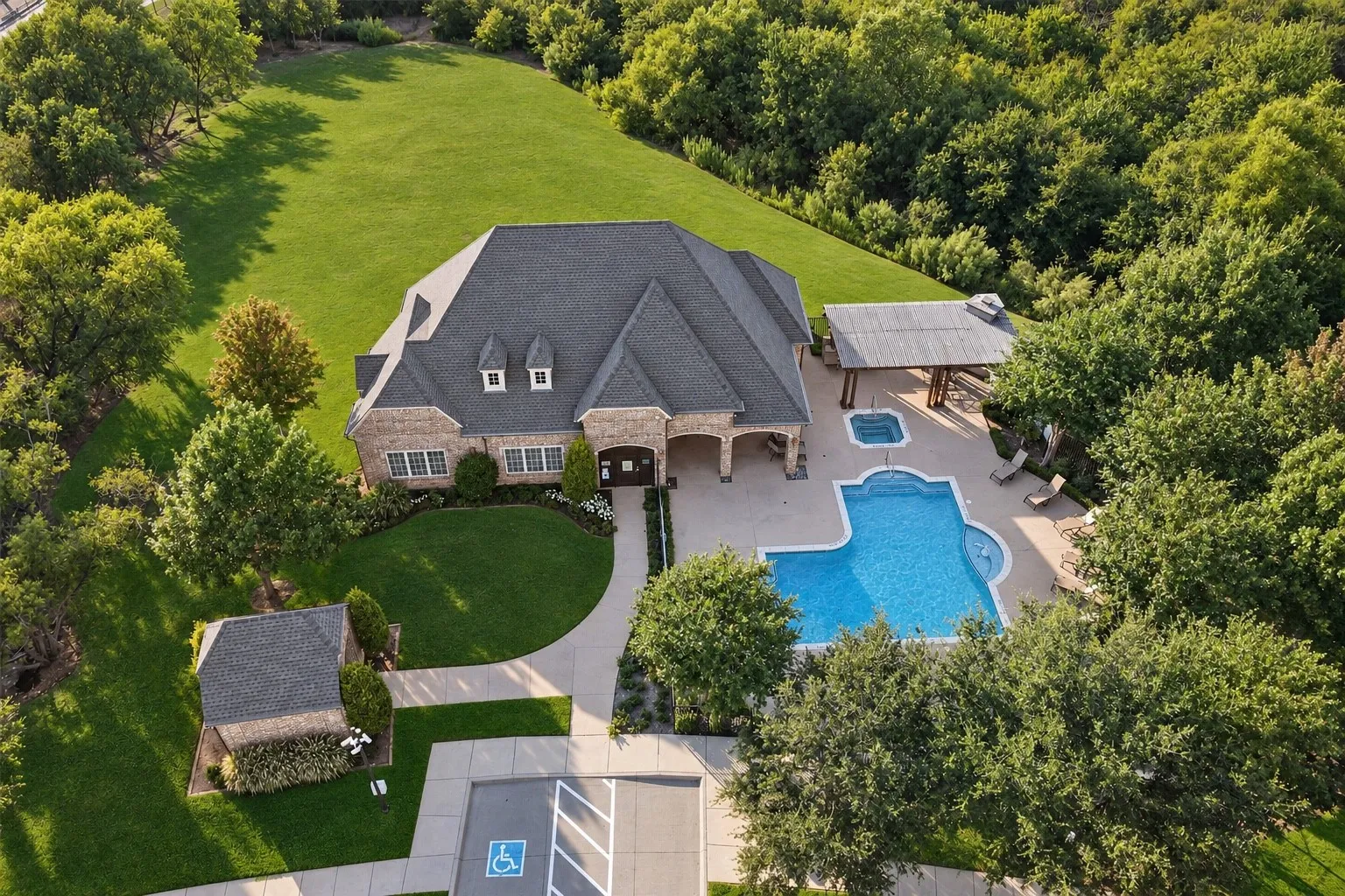 Stone exterior featuring a dark-toned roof, dormer windows, a swimming pool, and an attached hot tub