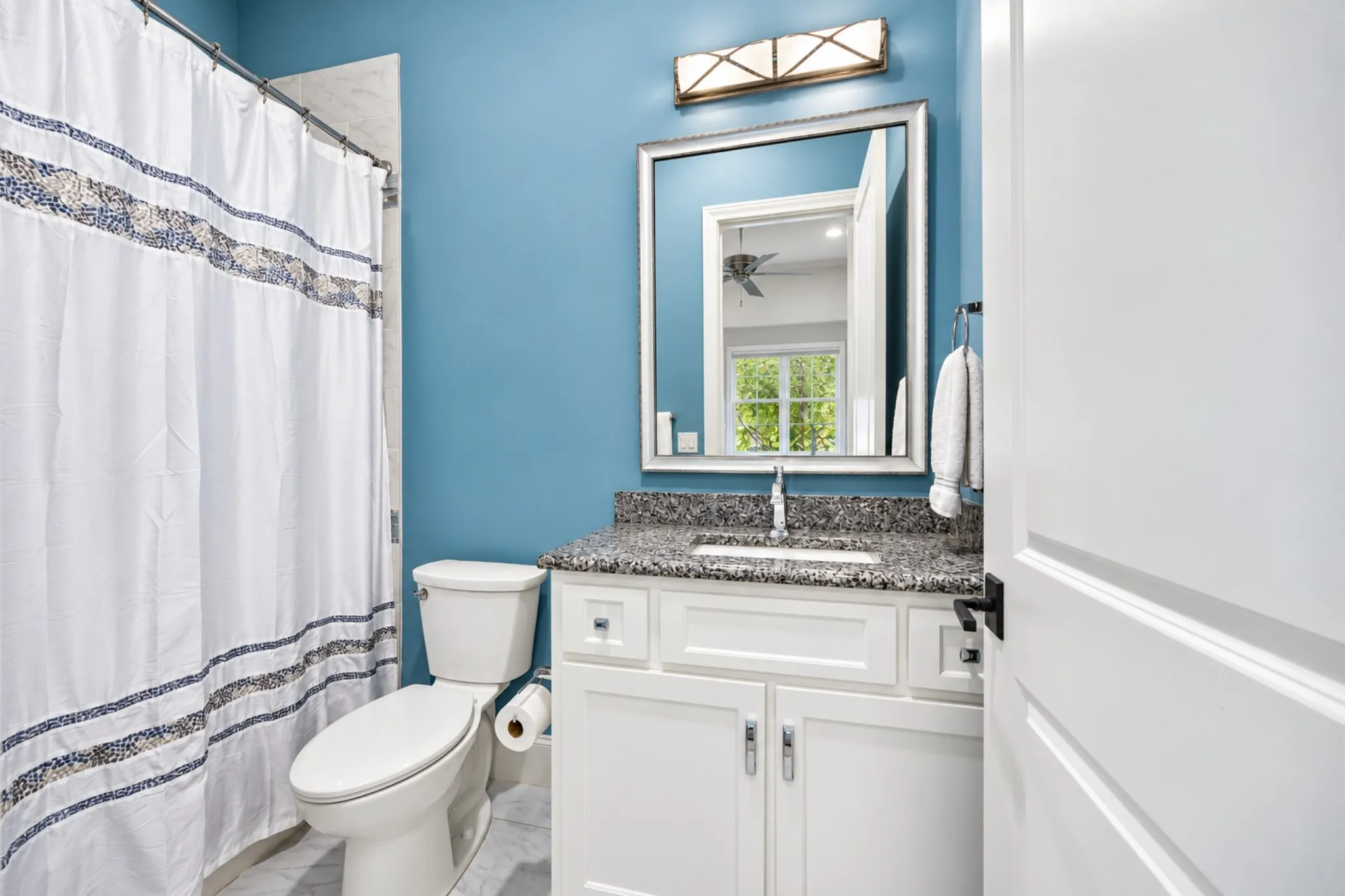 White vanity with a stone countertop, an undermount sink, and a framed mirror above