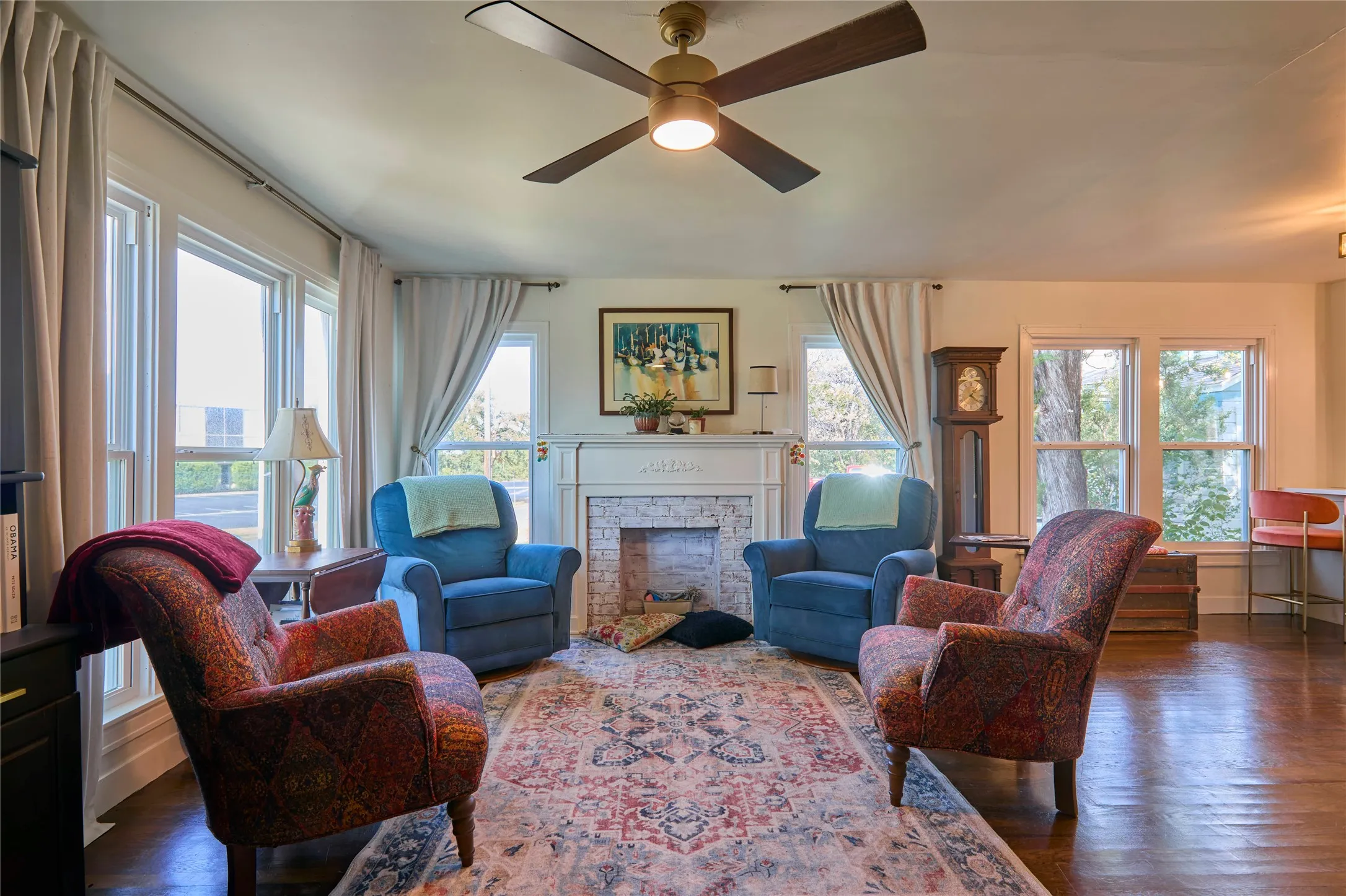 Hardwood flooring, ceiling fan with integrated lighting, multiple sash windows, white mantel, and brick-surround fireplace
