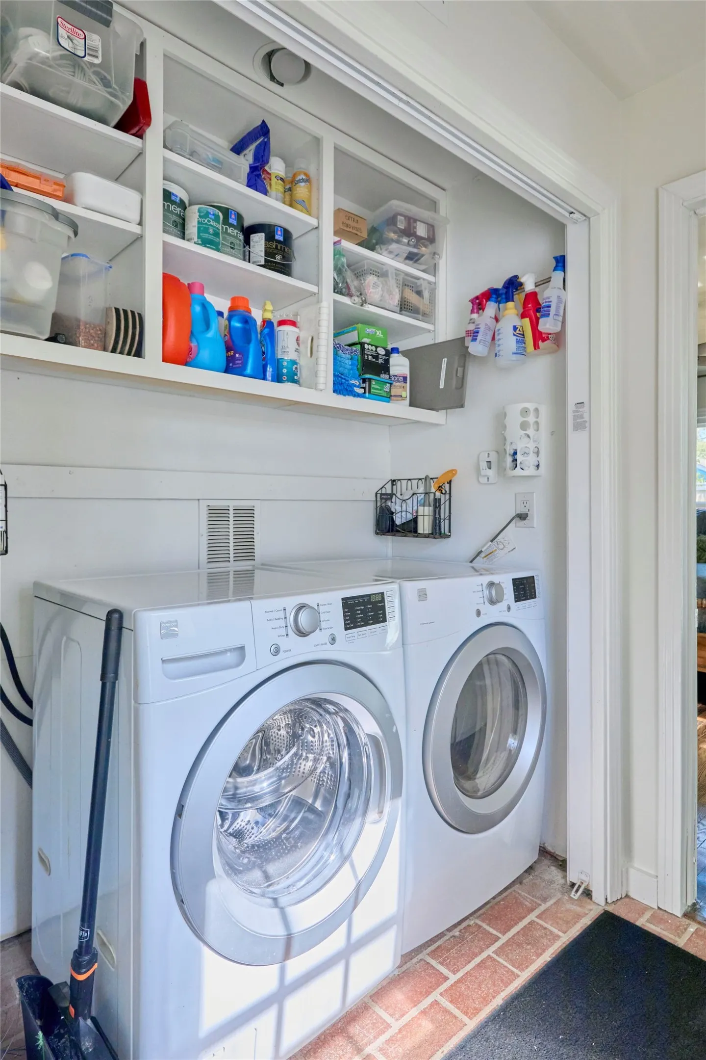 Built-in white cabinetry with open shelving, front-loading washer and dryer, brick-finish flooring, and white wall paneling