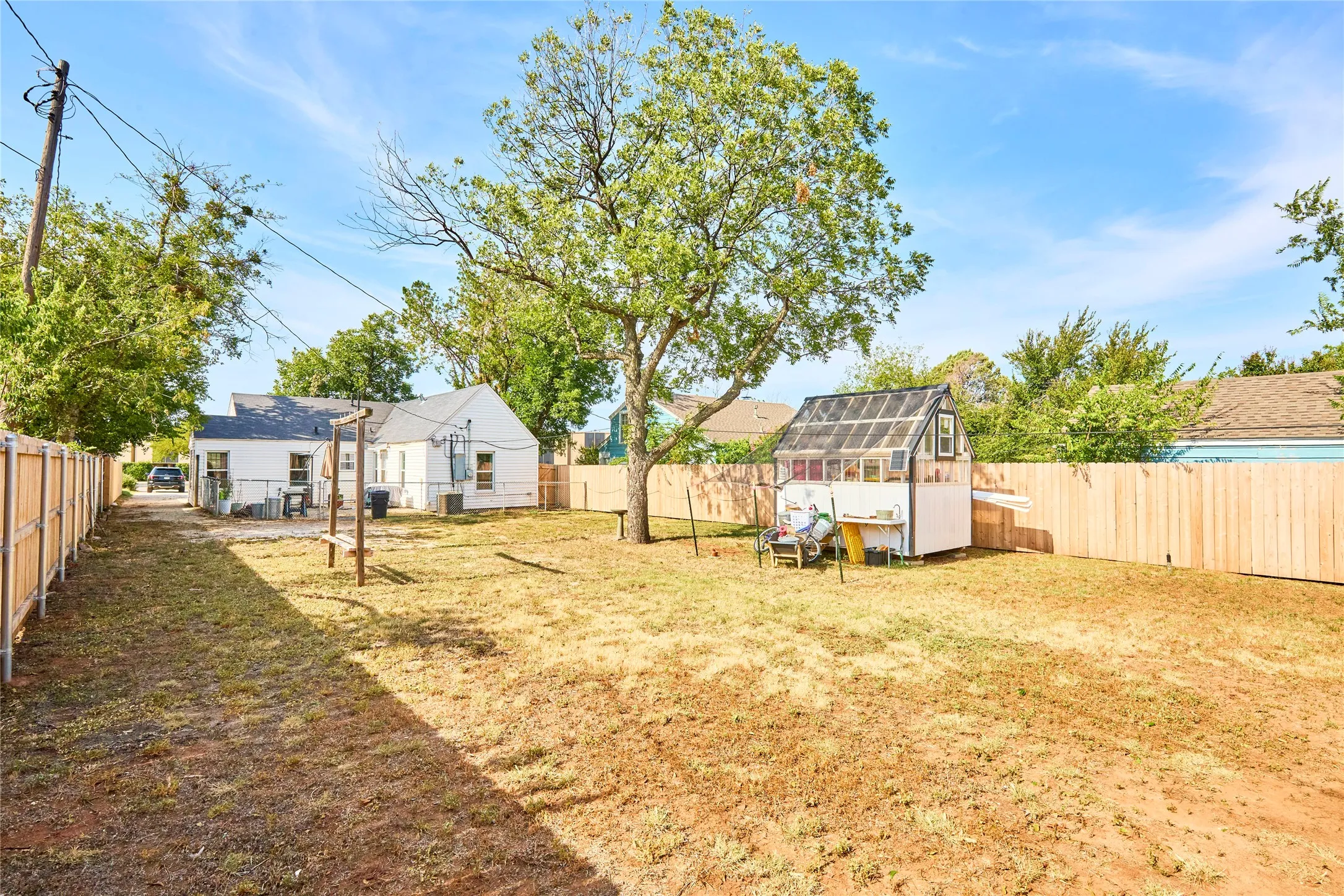 Expansive backyard with a wood privacy fence, mature trees, and a freestanding greenhouse structure