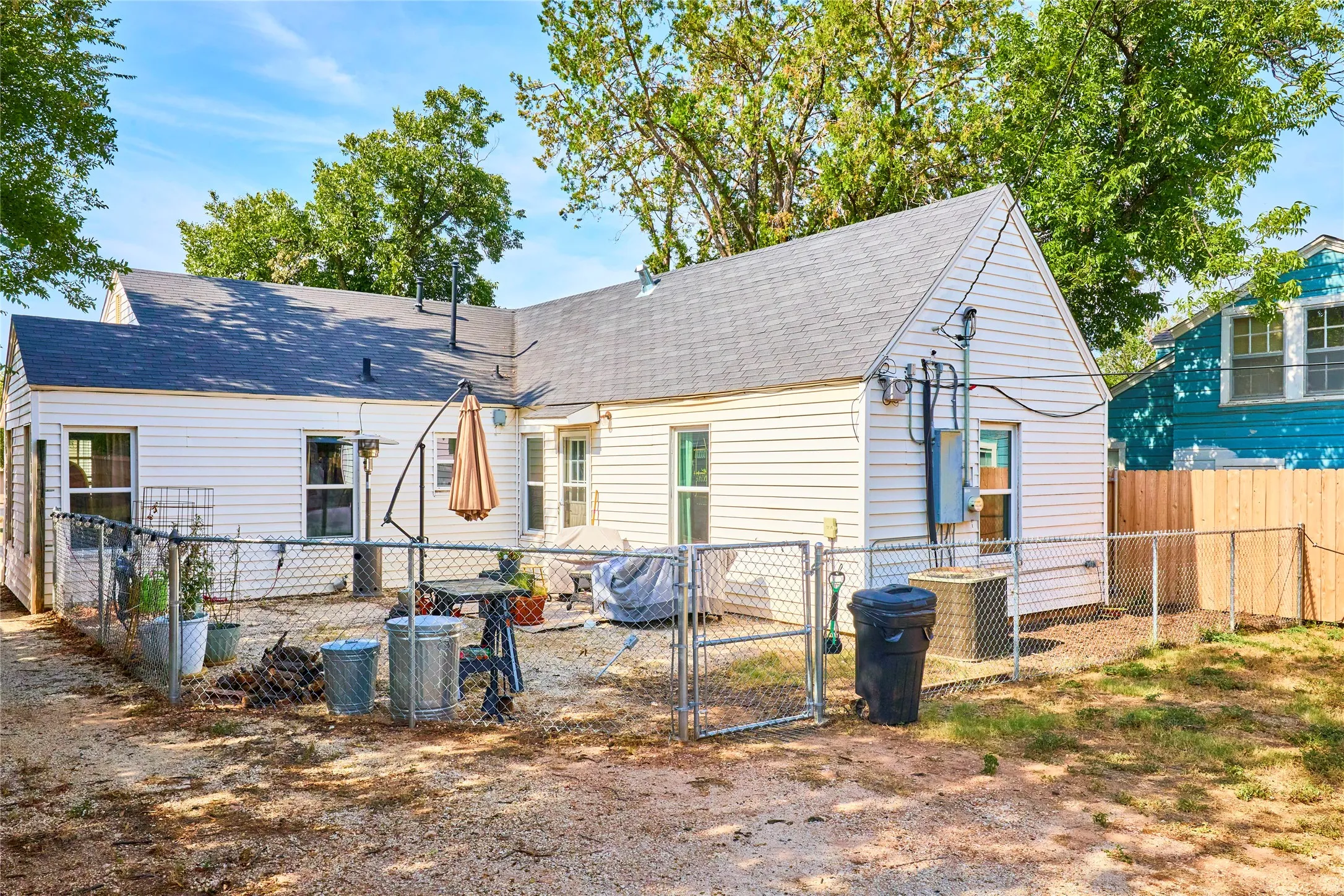 White siding exterior with a dark shingle roof, complemented by a chain-link fence